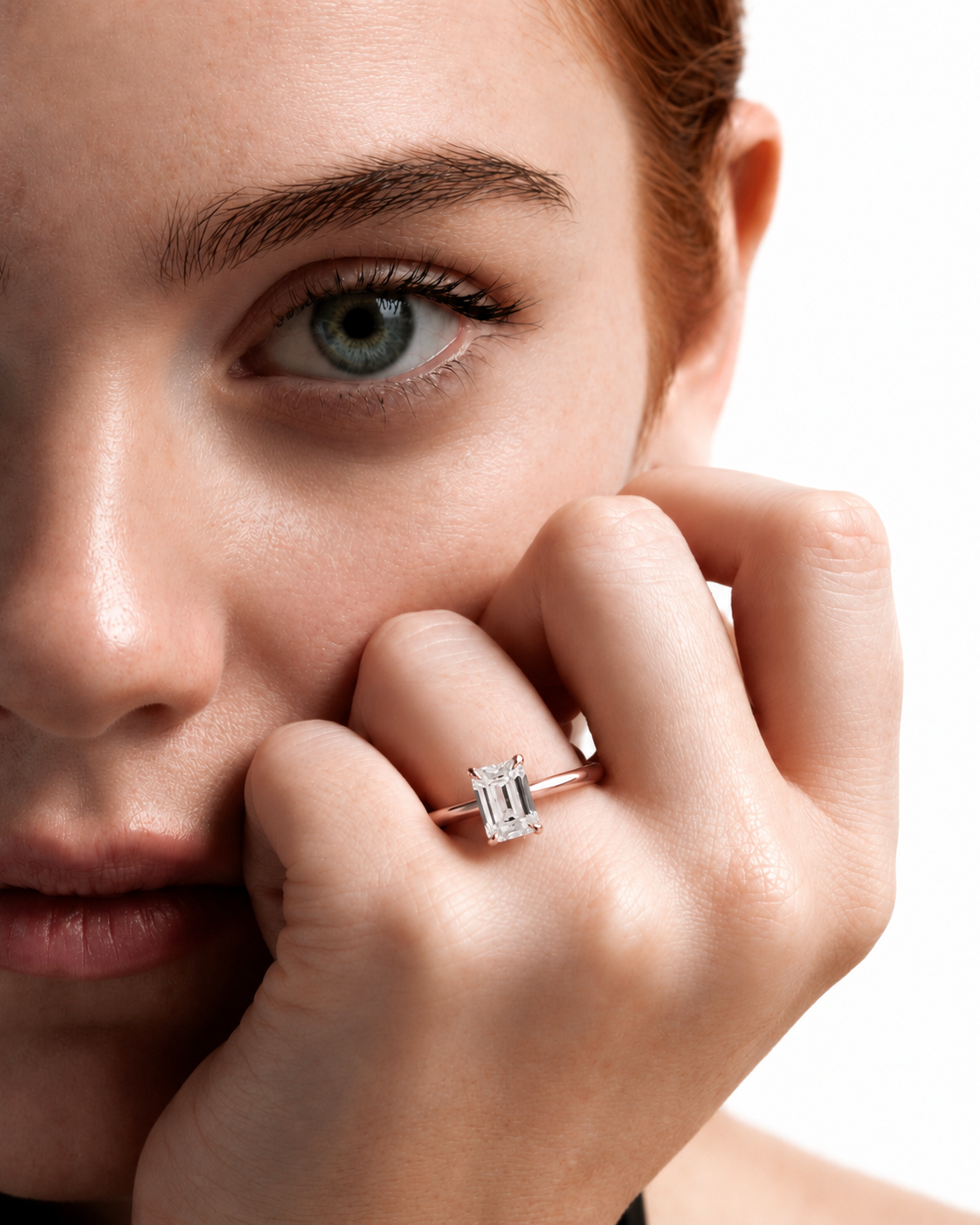 color_10K_RG, color_14K_RG &&
A close-up lifestyle shot of a woman wearing a silver emerald-cut diamond ring on her finger, with her hand resting near her cheek against a white background.
