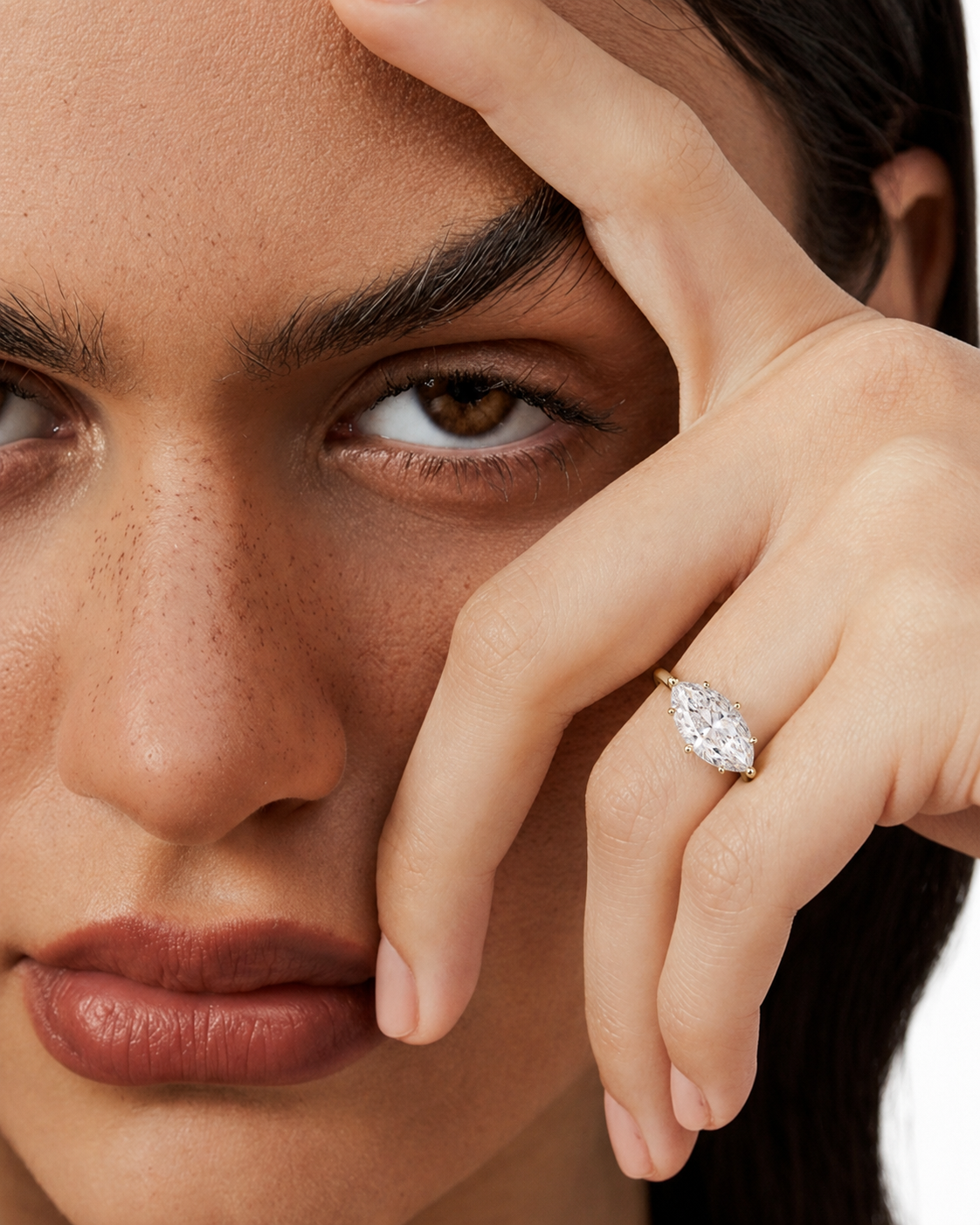 color_10K_YG, color_14K_YG &&Close-up of a model's face and hand wearing a marquise-cut diamond ring on a gold band.