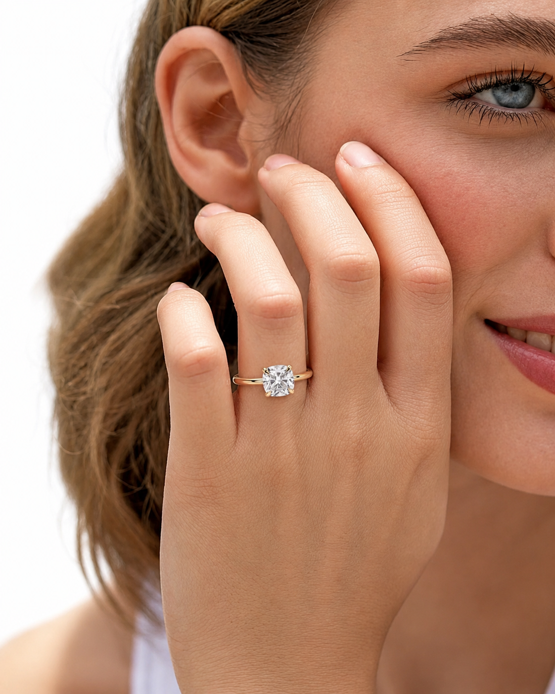 color_10K_YG, color_14K_YG &&A close-up lifestyle shot of a woman wearing a rose gold engagement ring with a round-cut clear gemstone on her finger, with her hand resting against her cheek against a white background.