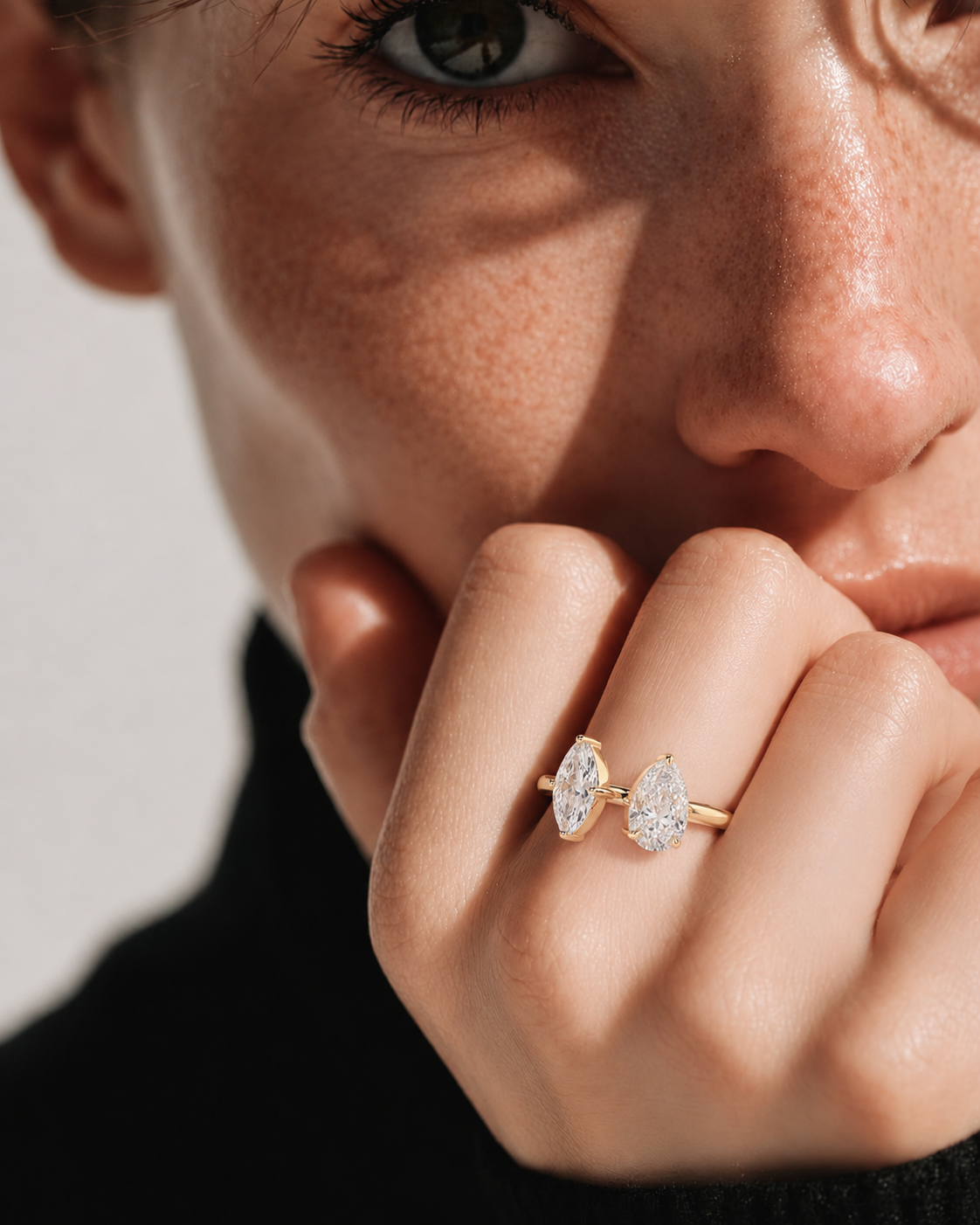 color_10K_YG, color_14K_YG &&A close-up lifestyle shot of a model wearing a gold ring with two marquise-cut clear gemstones on her finger, set against a neutral light gray background.