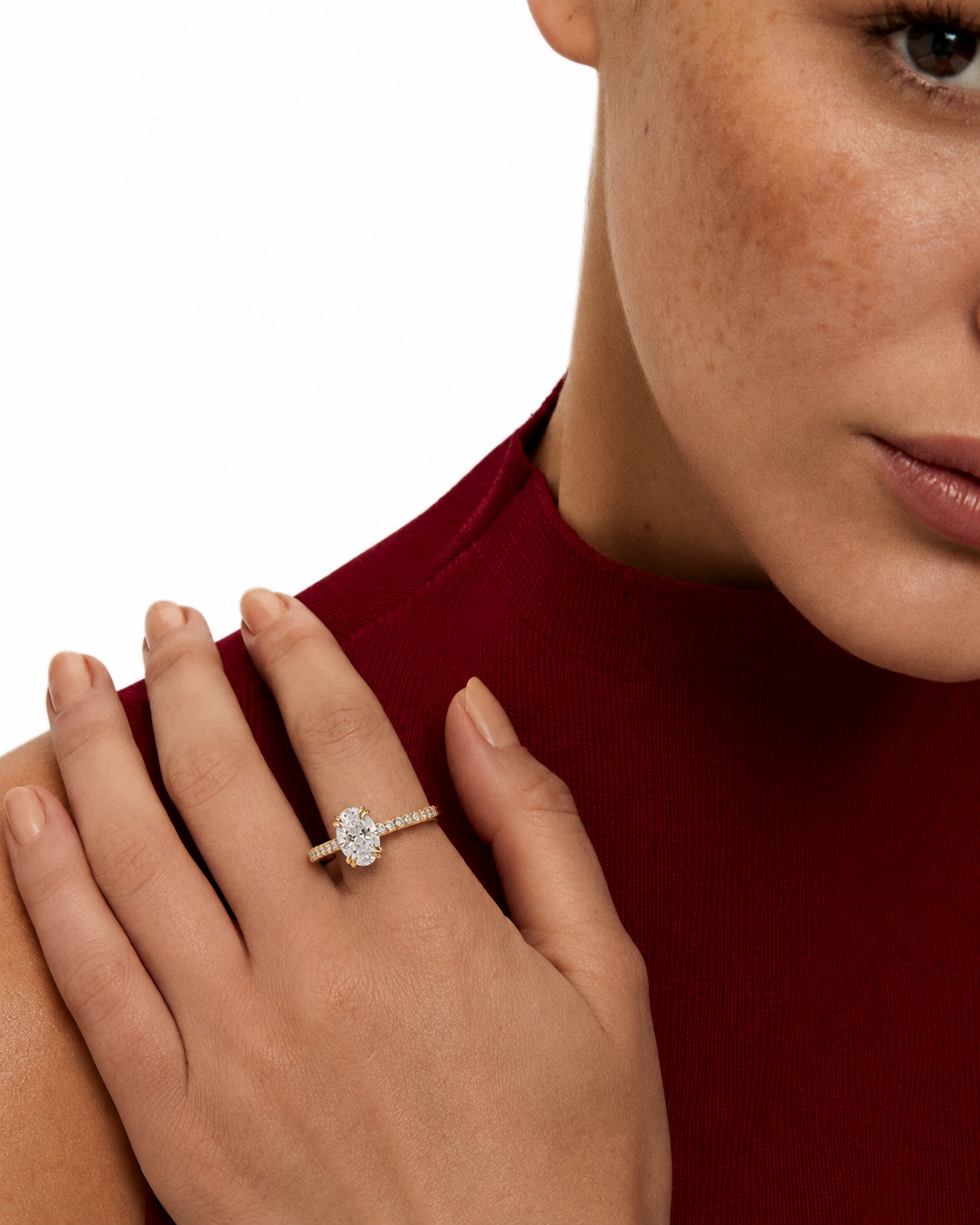 color_10K_YG, color_14K_YG &&A close-up lifestyle shot of a woman wearing a diamond engagement ring on her finger, dressed in a dark red ribbed top against a clean white background.