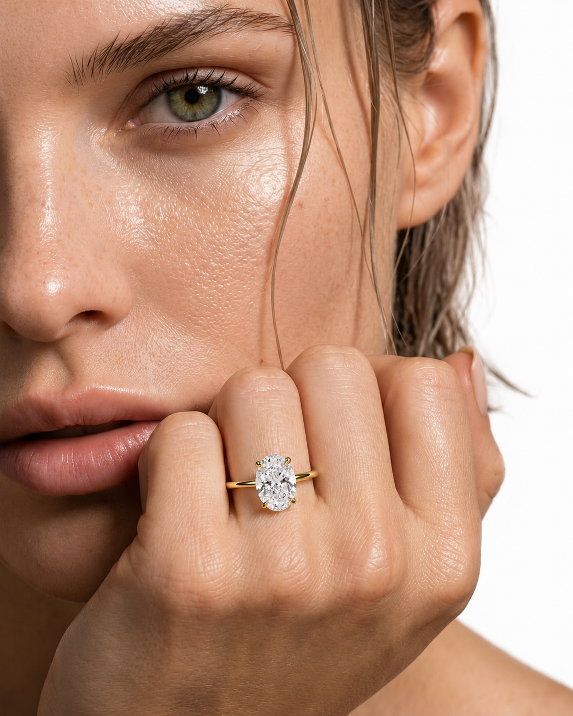 color_10K_YG, color_14K_YG &&A close-up lifestyle shot of a woman wearing a yellow gold engagement ring with a round brilliant-cut diamond. The ring is shown on her finger, with her hand resting near her chin against a clean white background.