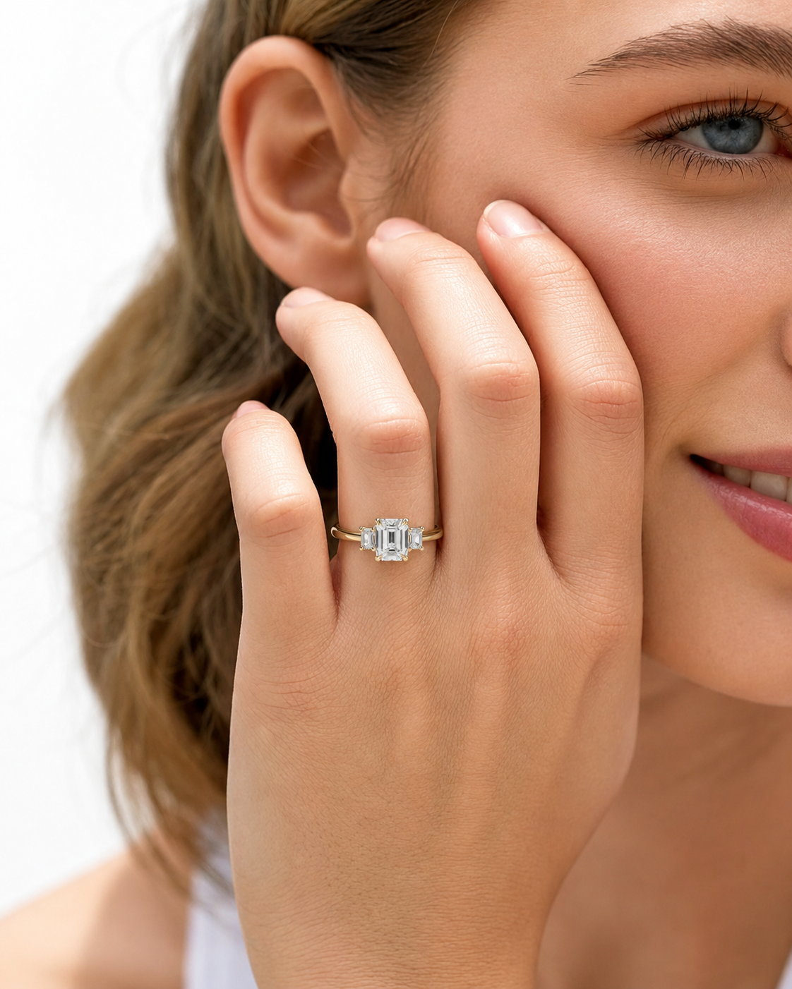 color_10K_YG, color_14K_YG &&A close-up lifestyle shot of a woman wearing a gold ring with a central baguette-cut diamond and smaller side diamonds on her finger.