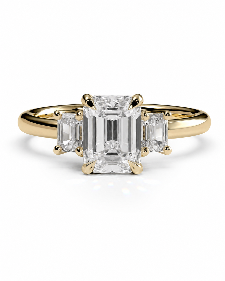 color_10K_YG, color_14K_YG &&A yellow gold three-stone ring featuring a large emerald-cut center diamond flanked by two smaller emerald-cut side diamonds, set against a clean white background.