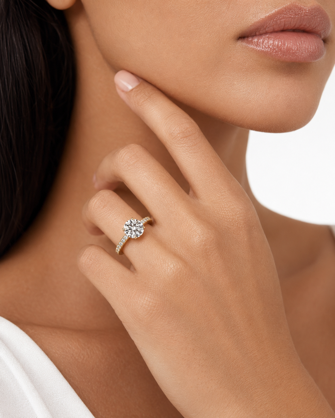 color_10K_YG, color_14K_YG &&A close-up lifestyle shot of a model wearing a diamond engagement ring on her finger. The ring features a round brilliant-cut center stone set in a yellow gold or white gold band with small accent stones.