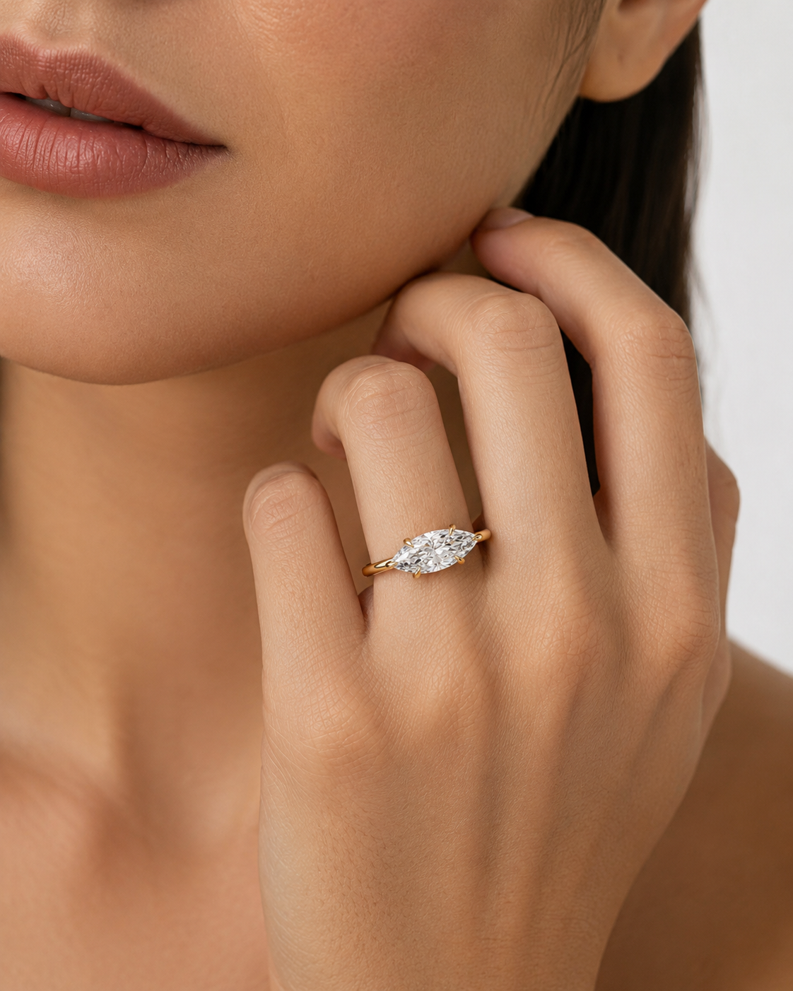 color_10K_YG, color_14K_YG &&A close-up lifestyle shot of a model wearing a yellow gold ring with a marquise-cut clear gemstone on her finger.