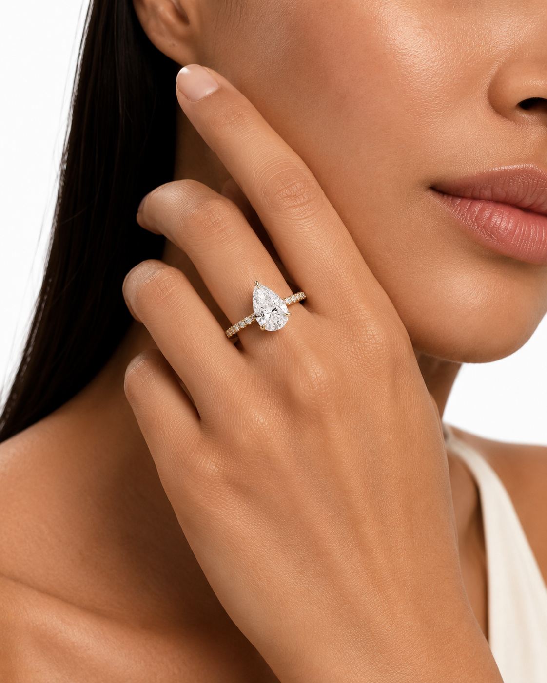 color_10K_YG, color_14K_YG &&A pear-cut diamond engagement ring on a slim band, worn on a model's ring finger. The model is shown in a close-up profile with her hand resting near her face against a clean white background.