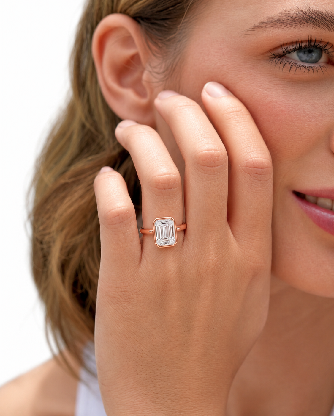 color_10K_RG, color_14K_RG &&
A close-up lifestyle shot of a woman wearing a rose gold ring with a large emerald-cut clear gemstone on her finger.