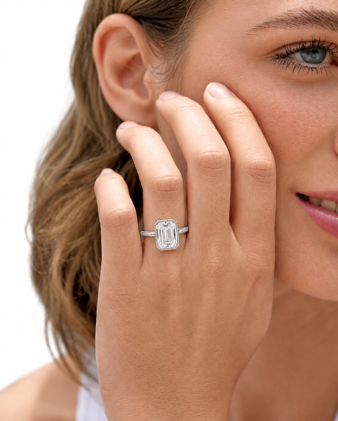color_925_SIL,color_935_ARG,color_10K_WG, color_14K_WG &&
A close-up lifestyle shot of a woman wearing a silver ring with an emerald-cut clear gemstone on her finger, with her hand resting against her cheek against a white background.