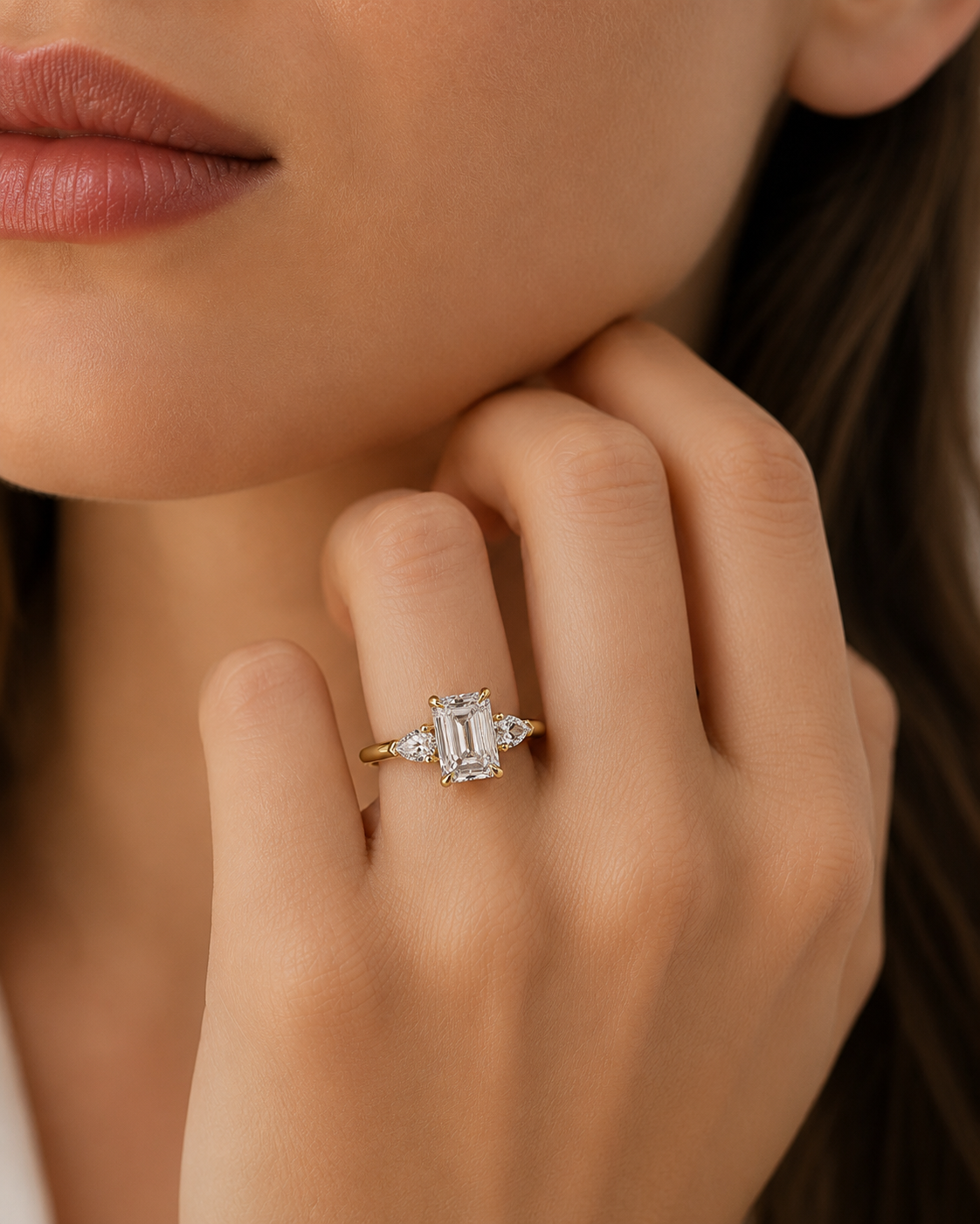 color_10K_YG, color_14K_YG &&A close-up of a model's hand wearing a yellow gold ring with an emerald-cut diamond center stone and small side diamonds.