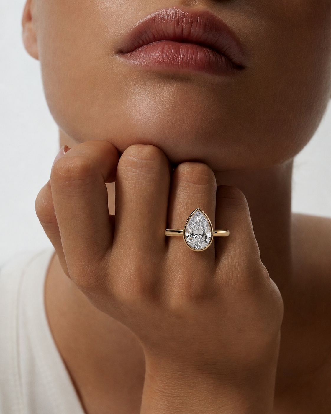 color_10K_YG, color_14K_YG &&A close-up of a model's hand resting on their chin, showcasing a gold ring with a pear-cut clear gemstone.