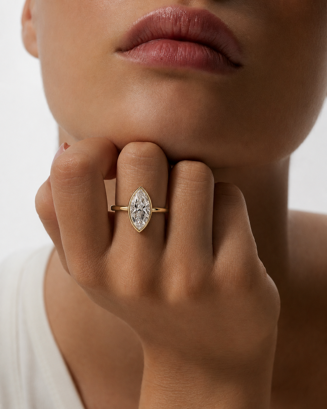 color_10K_YG, color_14K_YG &&A close-up lifestyle shot of a model wearing a gold ring with a marquise-cut clear gemstone on one finger, with her hand resting near her chin against a clean white background.