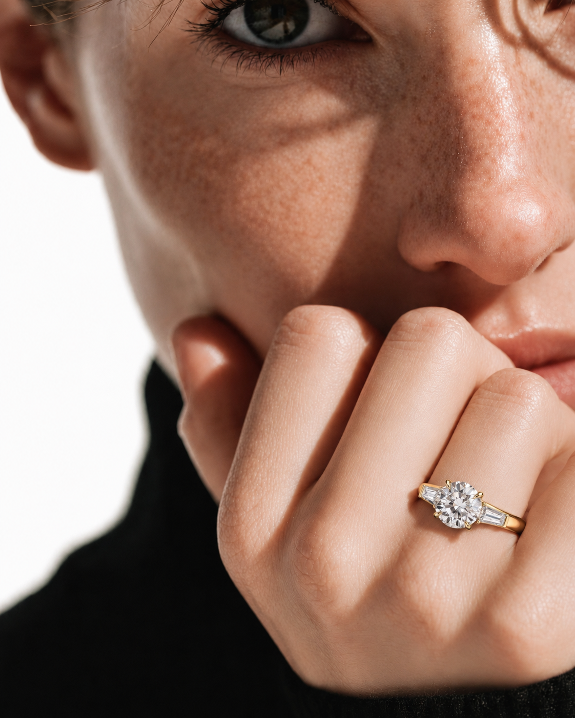 color_10K_YG, color_14K_YG &&A close-up lifestyle shot of a model wearing a yellow gold diamond engagement ring on her finger, with her hand resting near her chin against a bright white background.