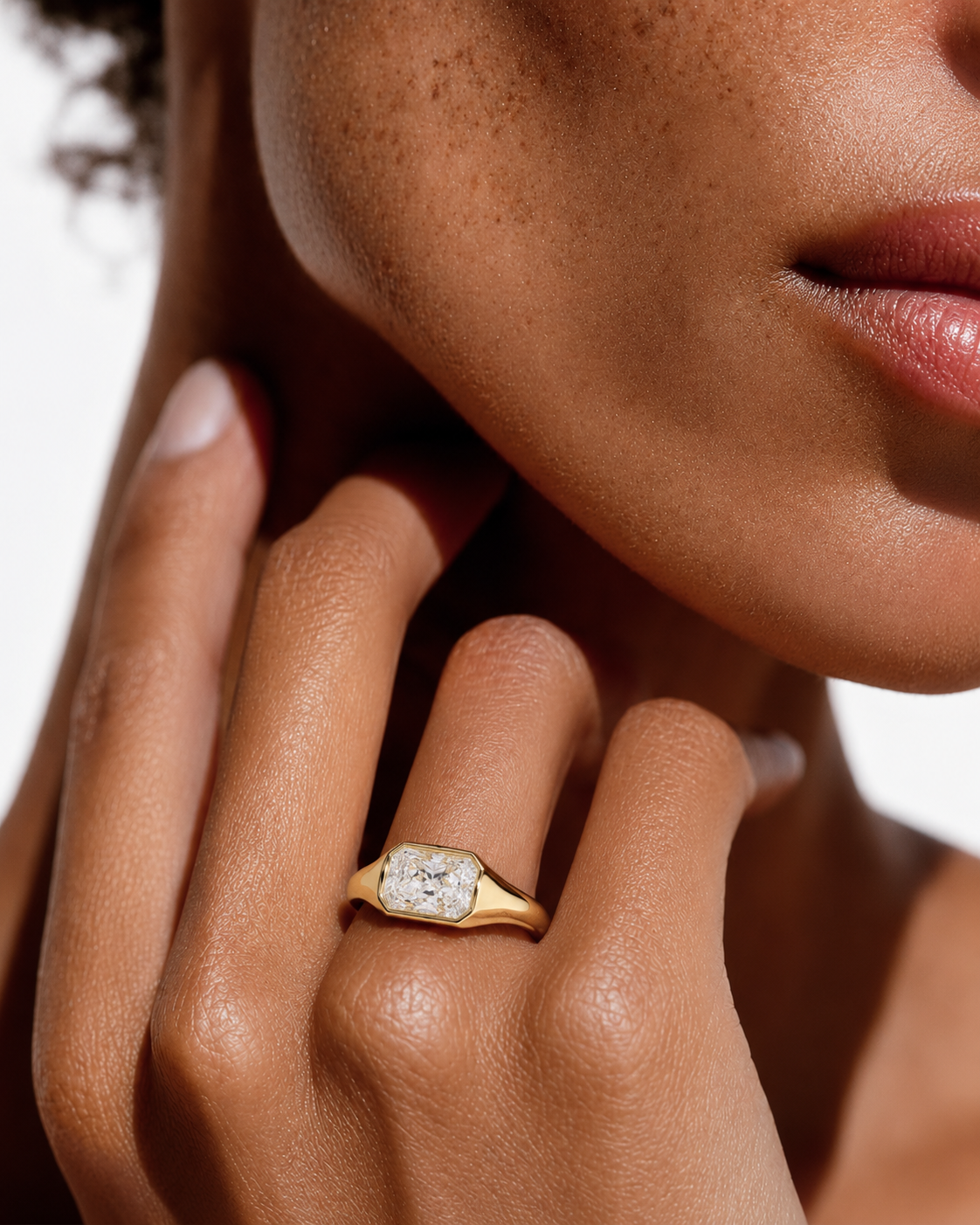 color_10K_YG, color_14K_YG &&A close-up lifestyle shot of a model wearing a yellow gold ring with a rectangular cushion-cut clear gemstone on her finger.
