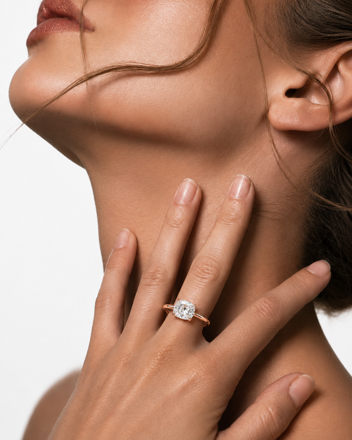 color_10K_RG, color_14K_RG &&
A close-up lifestyle shot of a woman wearing a rose gold ring with a round-cut clear gemstone on her finger, with her hand resting on her neck against a white background.