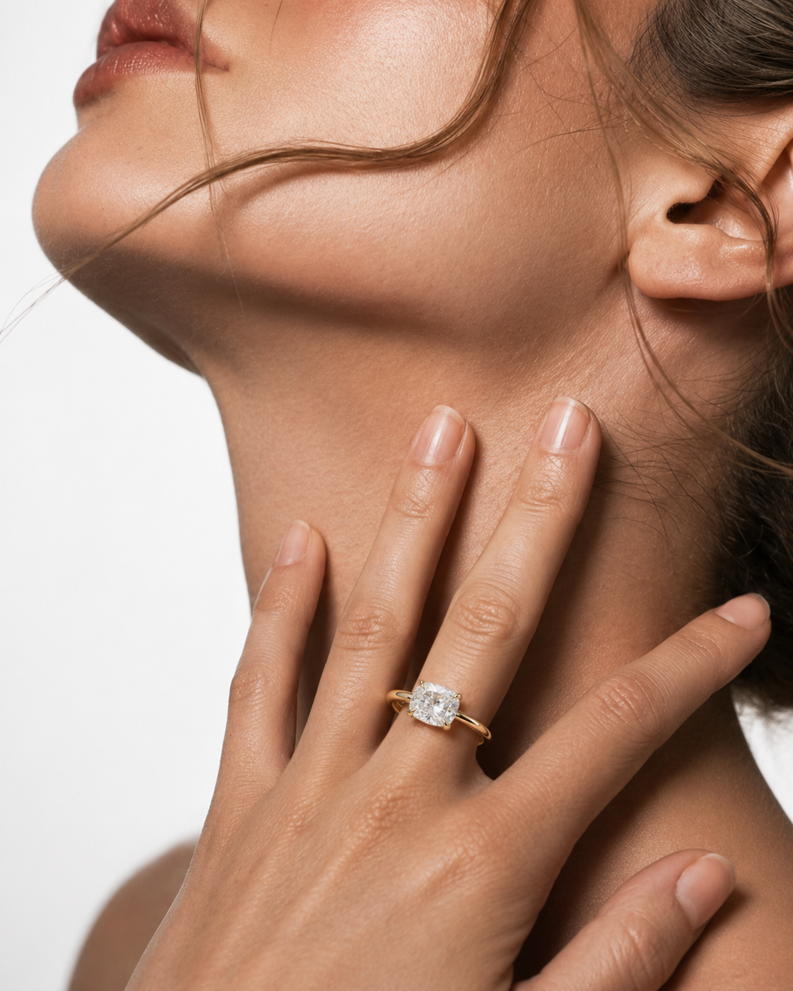 color_10K_YG, color_14K_YG &&
A close-up lifestyle shot of a model wearing a yellow gold ring with a square-cut clear gemstone on her finger, with her hand resting on her neck against a white background.