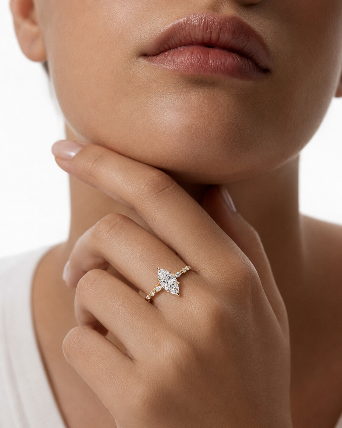 color_10K_YG, color_14K_YG &&A close-up lifestyle shot of a model wearing a delicate gold ring with a marquise-cut diamond cluster on the ring finger, set against a clean white background.