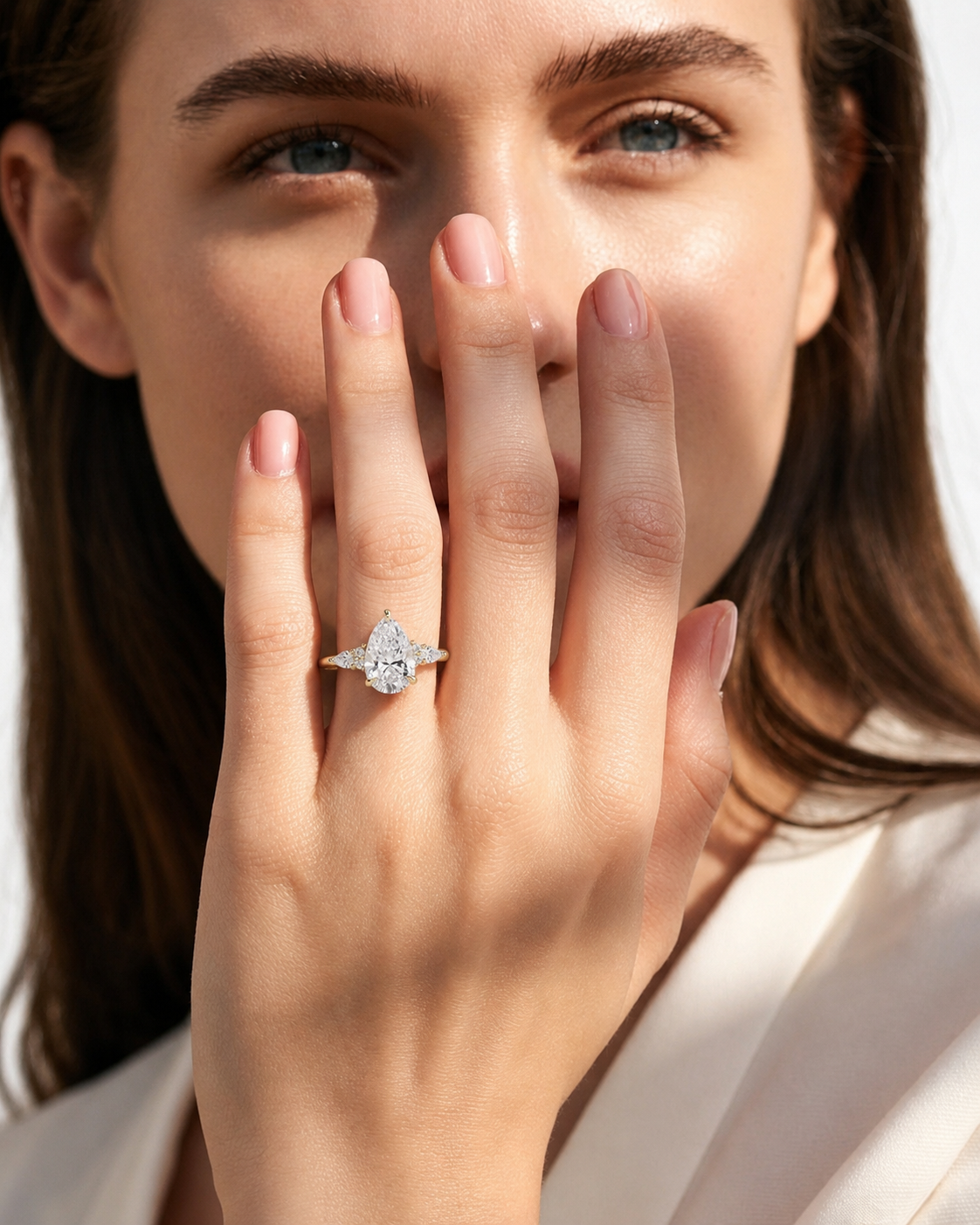 color_10K_YG, color_14K_YG &&A close-up lifestyle shot of a woman wearing a silver-toned ring with a marquise-cut diamond on her ring finger, with her hand covering part of her face.