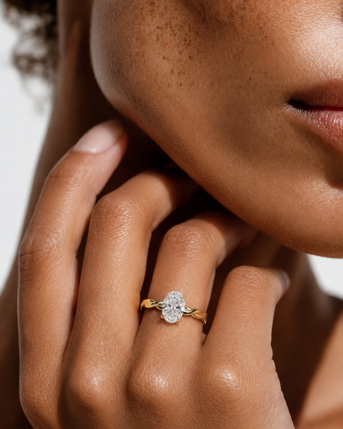 color_10K_YG, color_14K_YG &&
A close-up lifestyle shot of a model's hand wearing a yellow gold ring with a round-cut clear gemstone, set against a soft, warm-toned background.