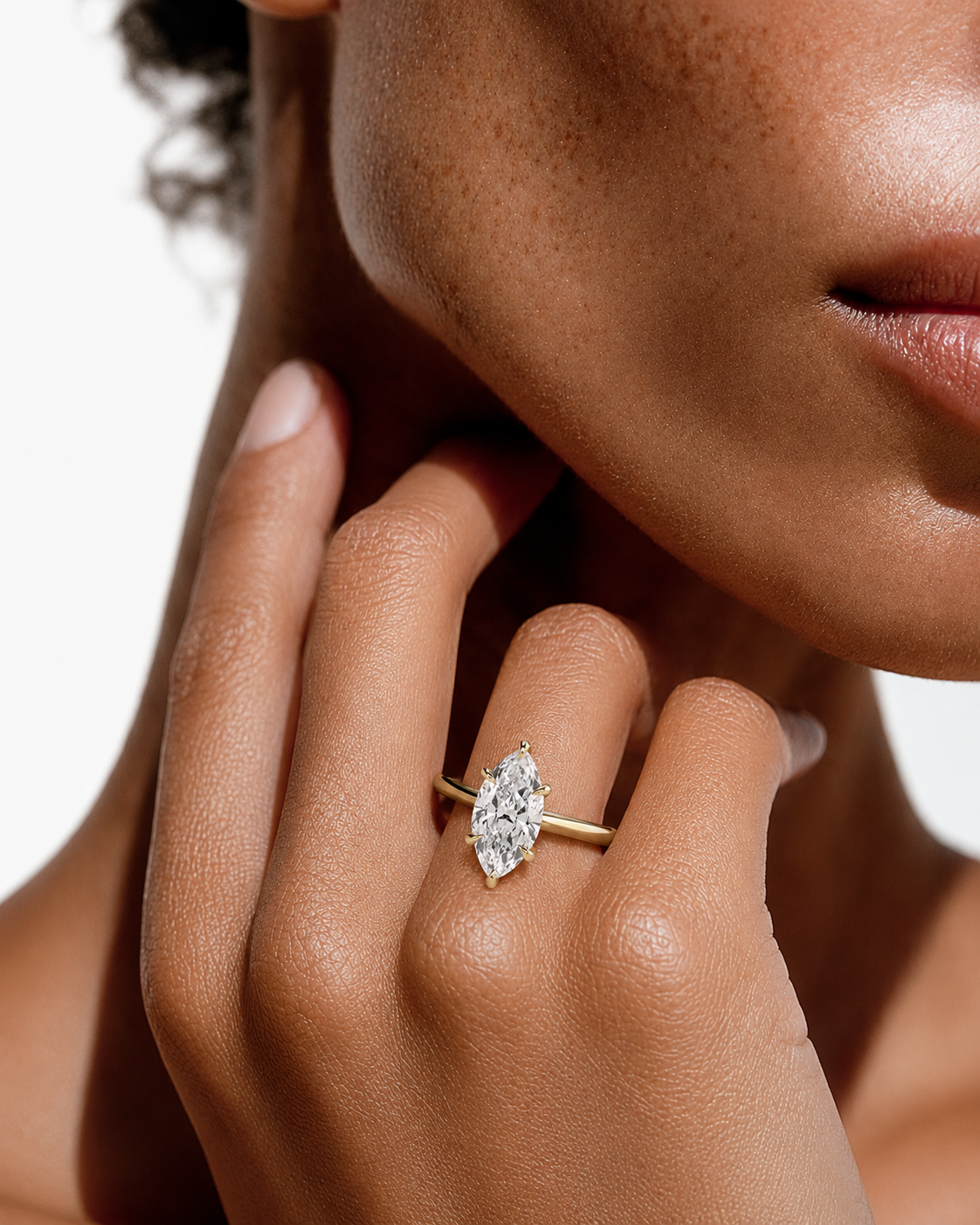 color_10K_YG, color_14K_YG &&A close-up lifestyle shot of a model wearing a yellow gold ring with a marquise-cut diamond on her finger. The ring is shown against her skin with a clean white background.