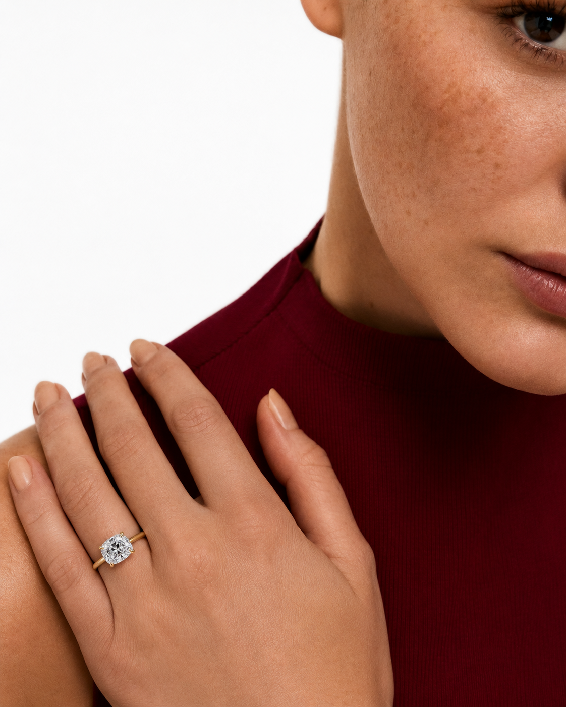 color_10K_YG, color_14K_YG &&A close-up lifestyle shot of a model wearing a diamond engagement ring on her finger, with her hand resting on her shoulder. She is wearing a deep burgundy top against a clean white background.