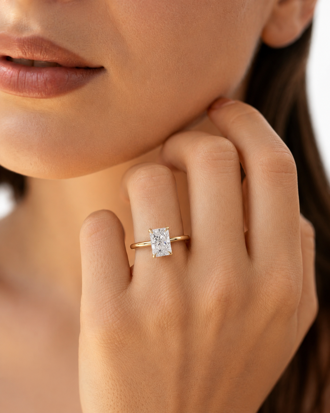color_10K_YG, color_14K_YG &&A close-up lifestyle shot of a model wearing a yellow gold ring with a rectangular clear gemstone on her finger.