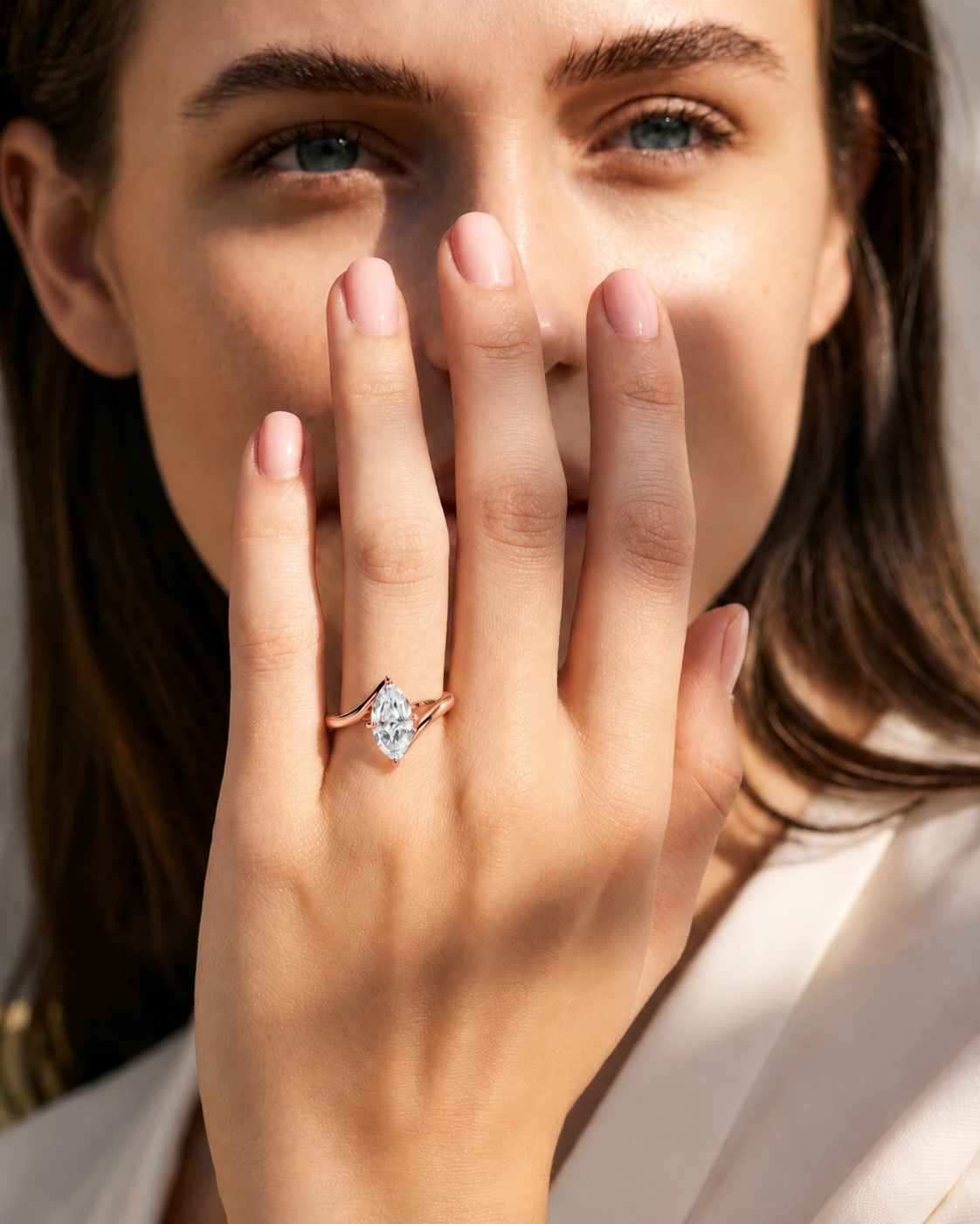 color_10K_RG, color_14K_RG &&
A close-up lifestyle shot of a woman wearing a delicate rose gold ring with a marquise-cut clear gemstone on her finger, with her hand covering part of her face.
