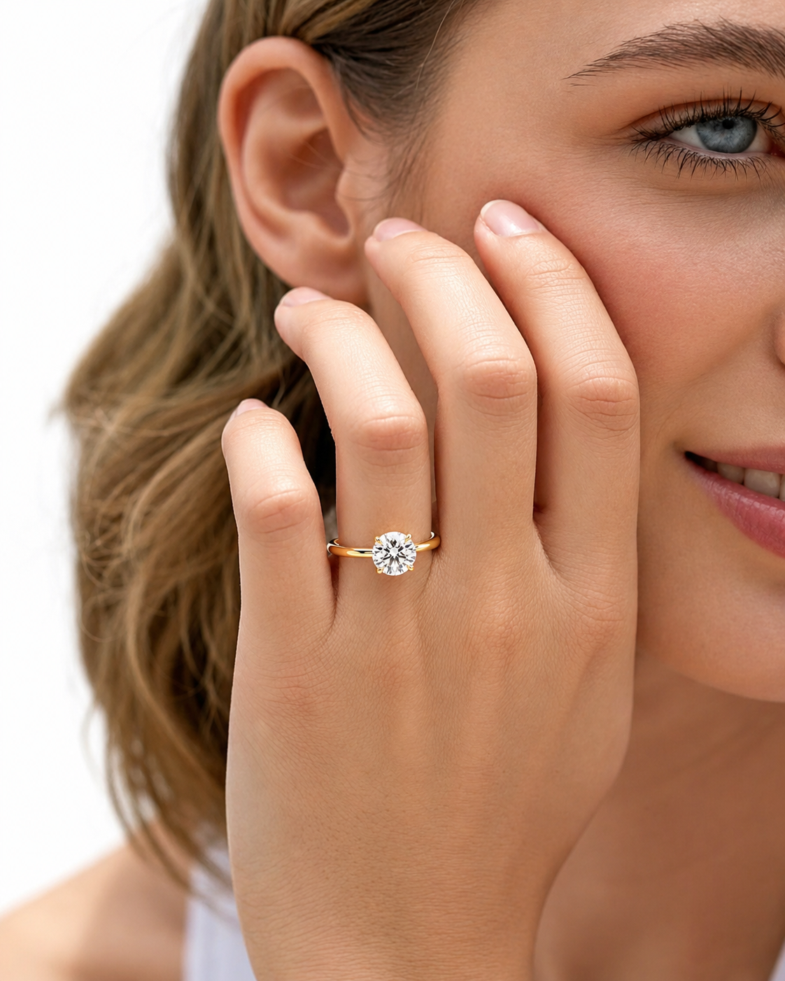 color_10K_YG, color_14K_YG &&A close-up lifestyle shot of a woman wearing a gold ring with a round-cut clear gemstone on her finger, with her hand resting against her cheek against a clean white background.