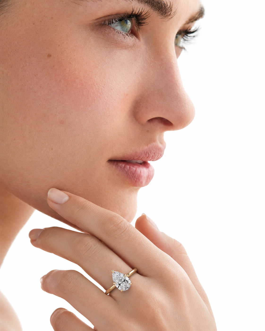color_10K_YG, color_14K_YG &&A close-up side profile of a woman wearing a gold ring with a pear-cut clear gemstone on her finger, set against a bright white background.