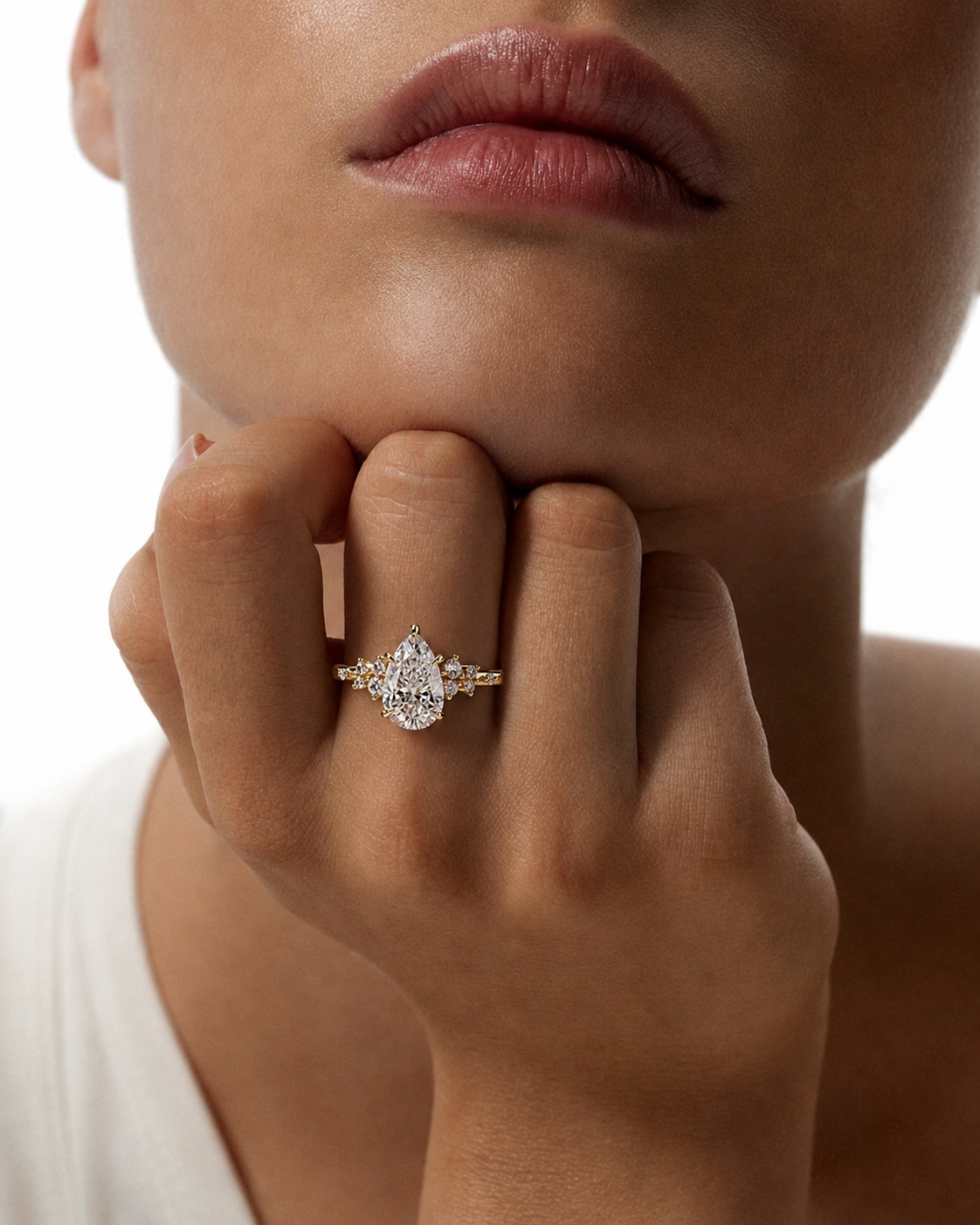 color_10K_YG, color_14K_YG &&A close-up lifestyle shot of a model wearing a gold ring with a pear-cut clear center stone and smaller surrounding stones on the ring finger.