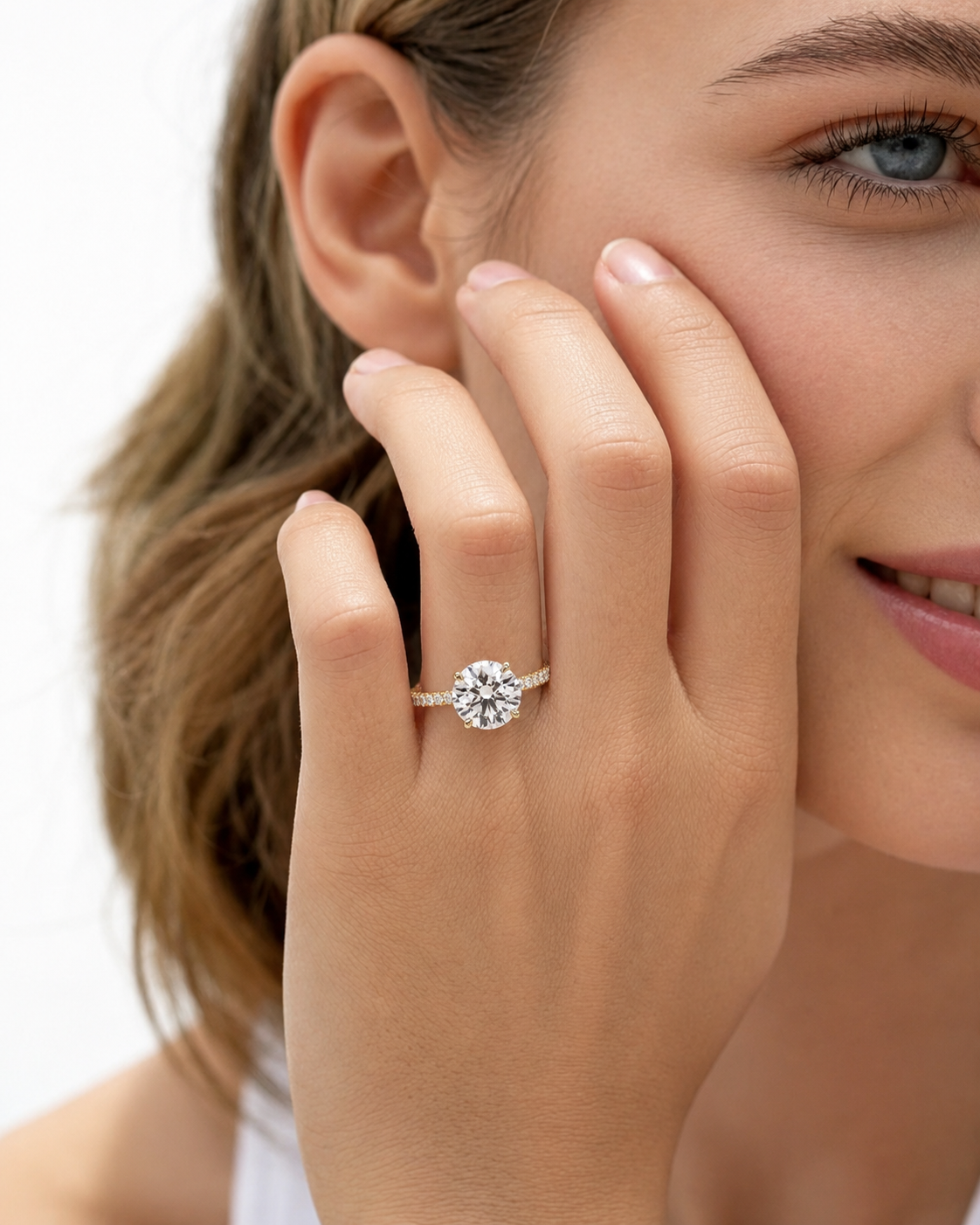 color_10K_YG, color_14K_YG &&
A close-up lifestyle shot of a woman wearing a round-cut diamond engagement ring on a silver band, with her hand resting against her cheek.