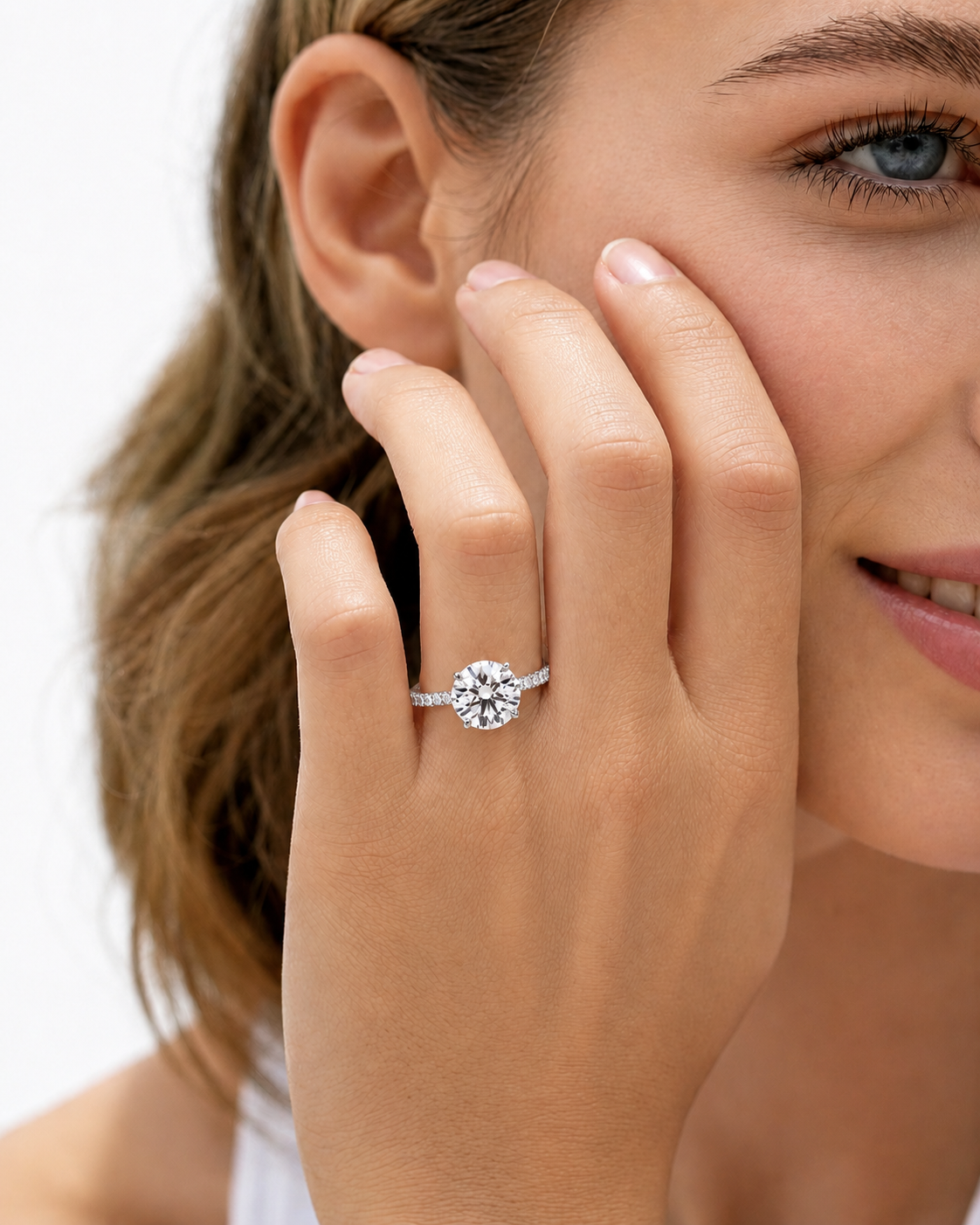 color_925_SIL,color_935_ARG,color_10K_WG, color_14K_WG &&
A close-up lifestyle shot of a woman wearing a silver-toned diamond engagement ring on her finger, with her hand resting against her cheek against a clean white background.