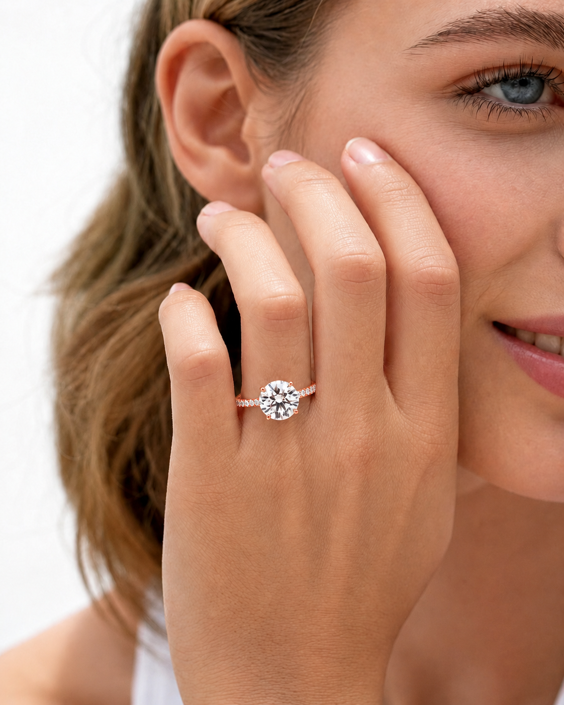 color_10K_RG, color_14K_RG &&
A close-up lifestyle shot of a woman wearing a round-cut diamond engagement ring on a silver band, with her hand resting against her cheek.