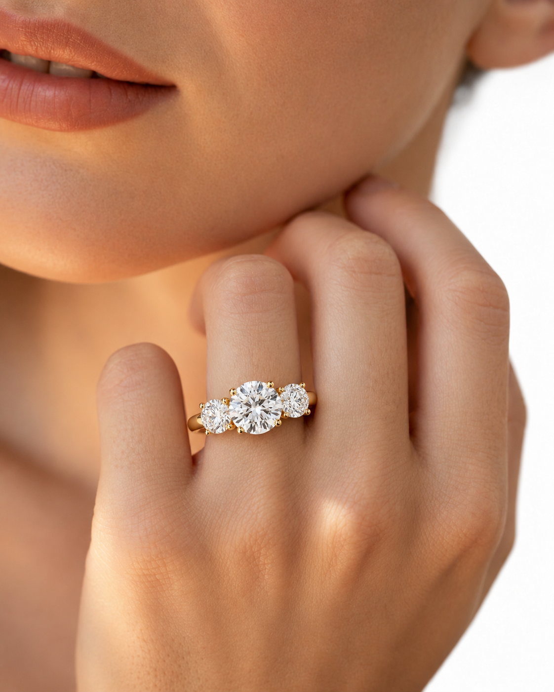color_10K_YG, color_14K_YG &&A close-up lifestyle shot of a model's hand wearing a yellow gold three-stone ring with sparkling clear gemstones, set against a clean white background.