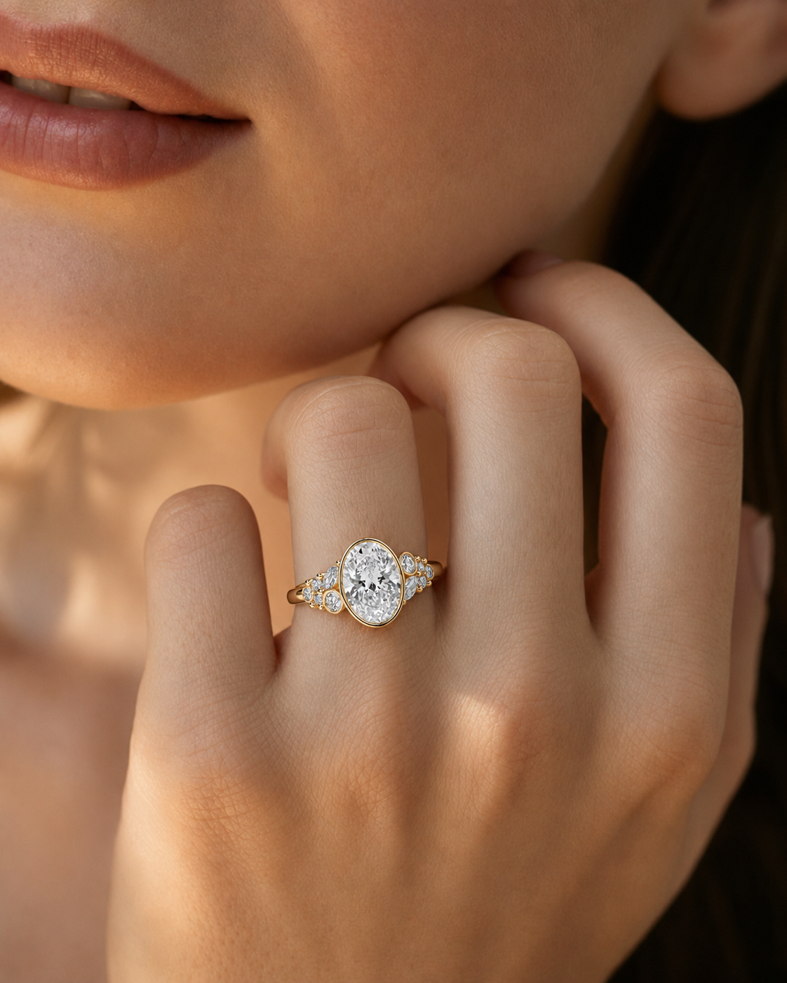 color_10K_YG, color_14K_YG &&A close-up lifestyle shot of a model's hand wearing a gold ring with a central oval-cut diamond and smaller surrounding diamonds.