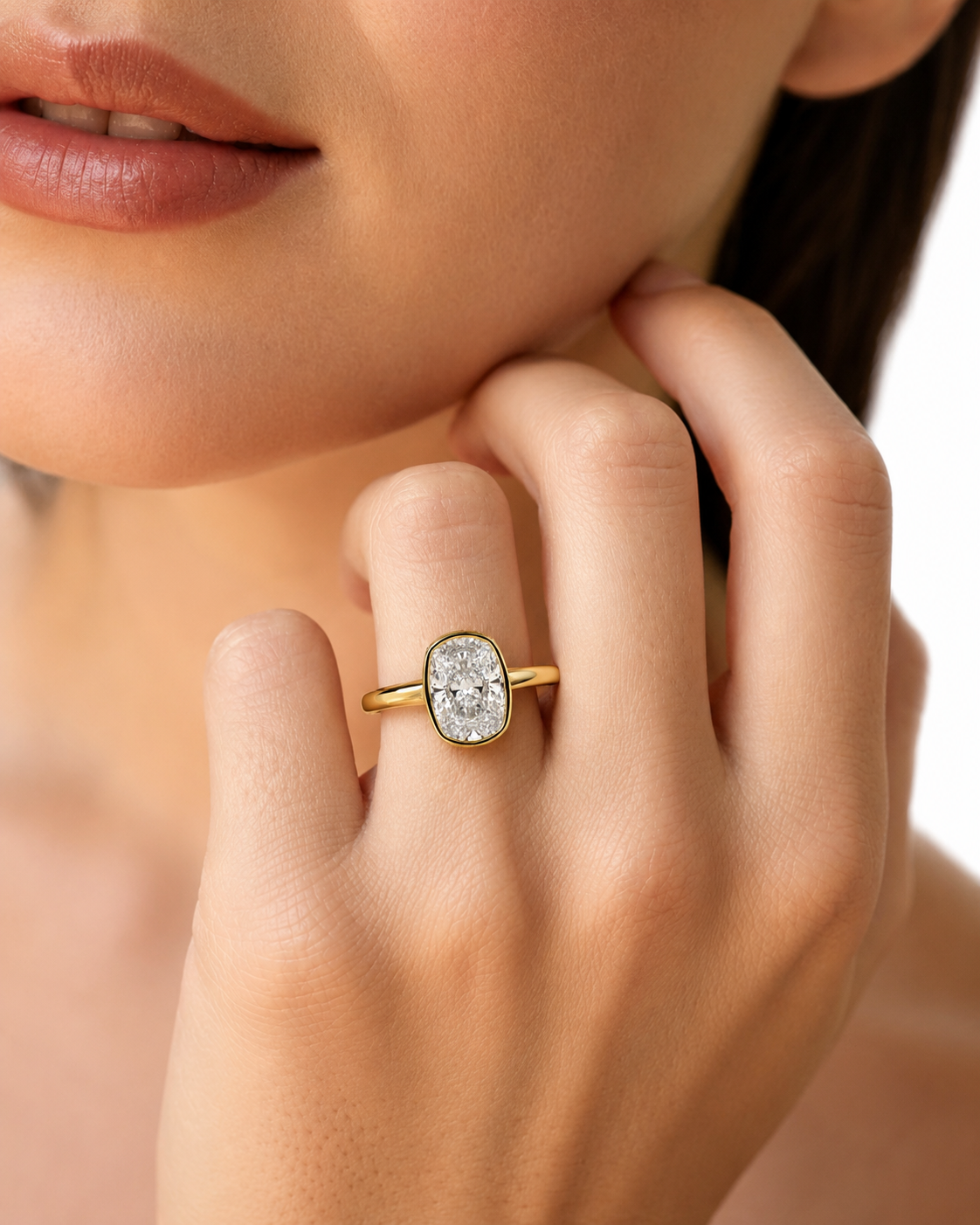 color_10K_YG, color_14K_YG &&A close-up lifestyle shot of a model wearing a gold ring with a cushion-cut clear gemstone on her finger.