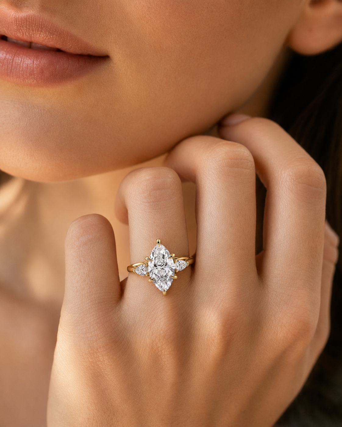 color_10K_YG, color_14K_YG &&A close-up lifestyle shot of a model's hand wearing a yellow gold ring with a marquise-cut diamond center stone and smaller round diamonds on the shoulders.