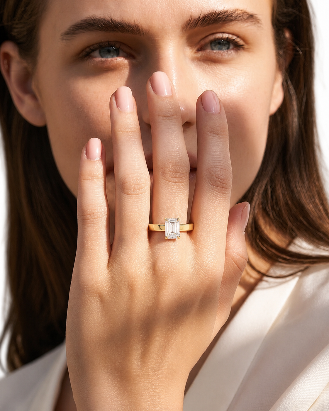 color_10K_YG, color_14K_YG &&A close-up lifestyle shot of a woman wearing a yellow gold ring with a rectangular baguette-cut clear gemstone on her finger, holding her hand near her face.