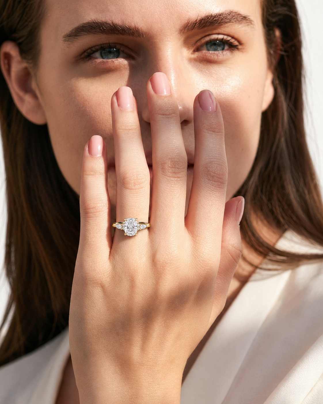 color_10K_YG, color_14K_YG &&A close-up lifestyle shot of a woman wearing a yellow gold ring with a round-cut clear gemstone, held up by her hand against a bright, soft background.