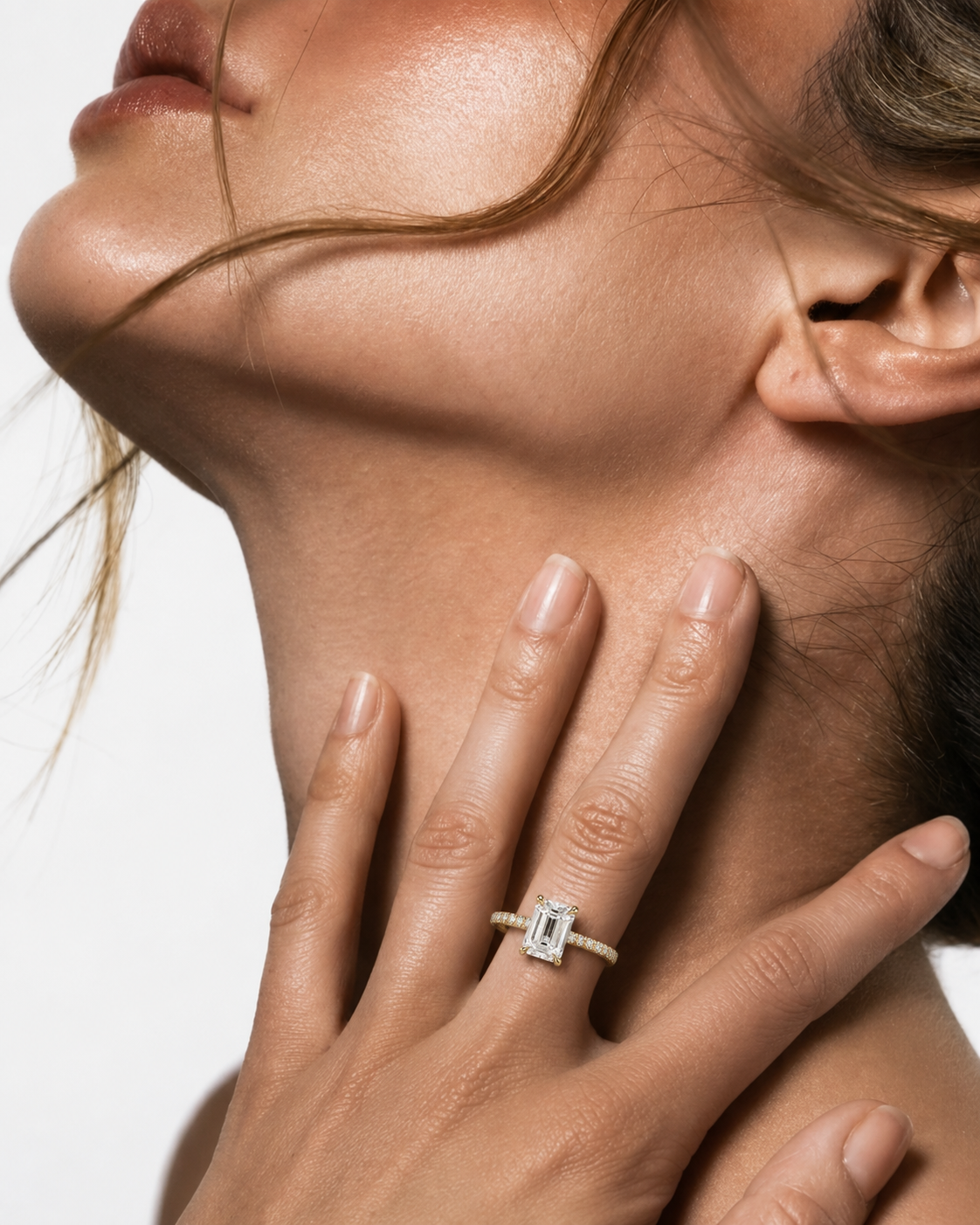 color_10K_YG, color_14K_YG &&A close-up lifestyle shot of a model's neck and hand, wearing a silver ring with a rectangular emerald-cut diamond on the ring finger. The background is a clean, solid white.
