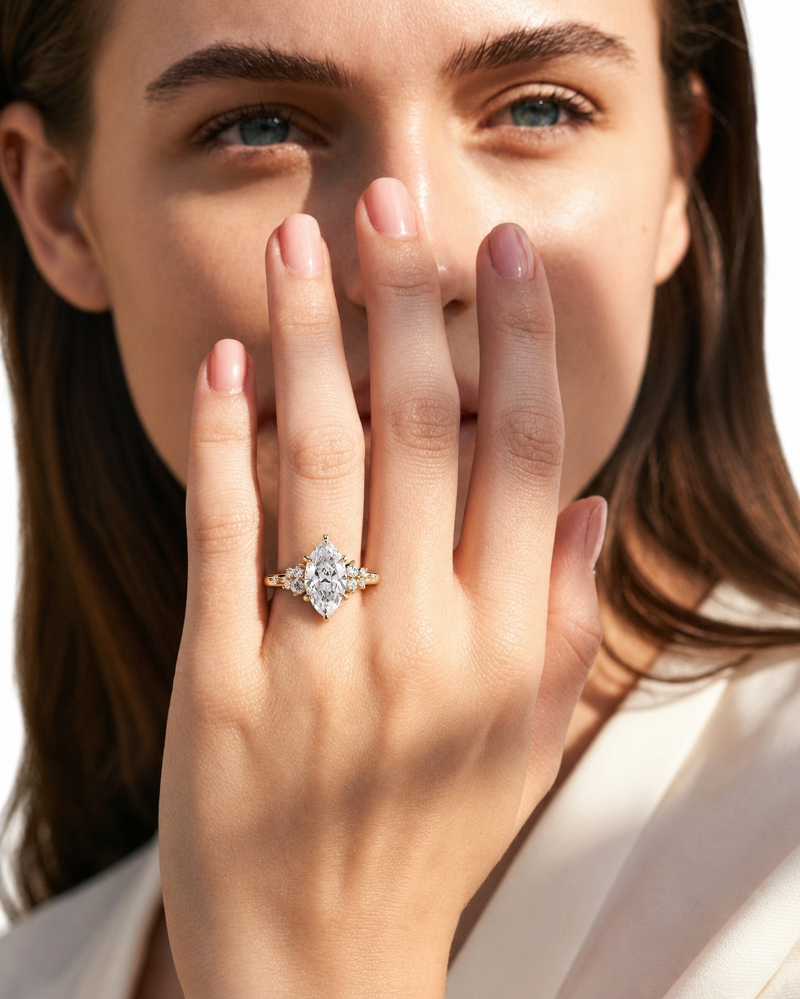 color_10K_YG, color_14K_YG &&A close-up lifestyle shot of a woman wearing a diamond ring with a gold band, holding her hand near her face against a bright white background.