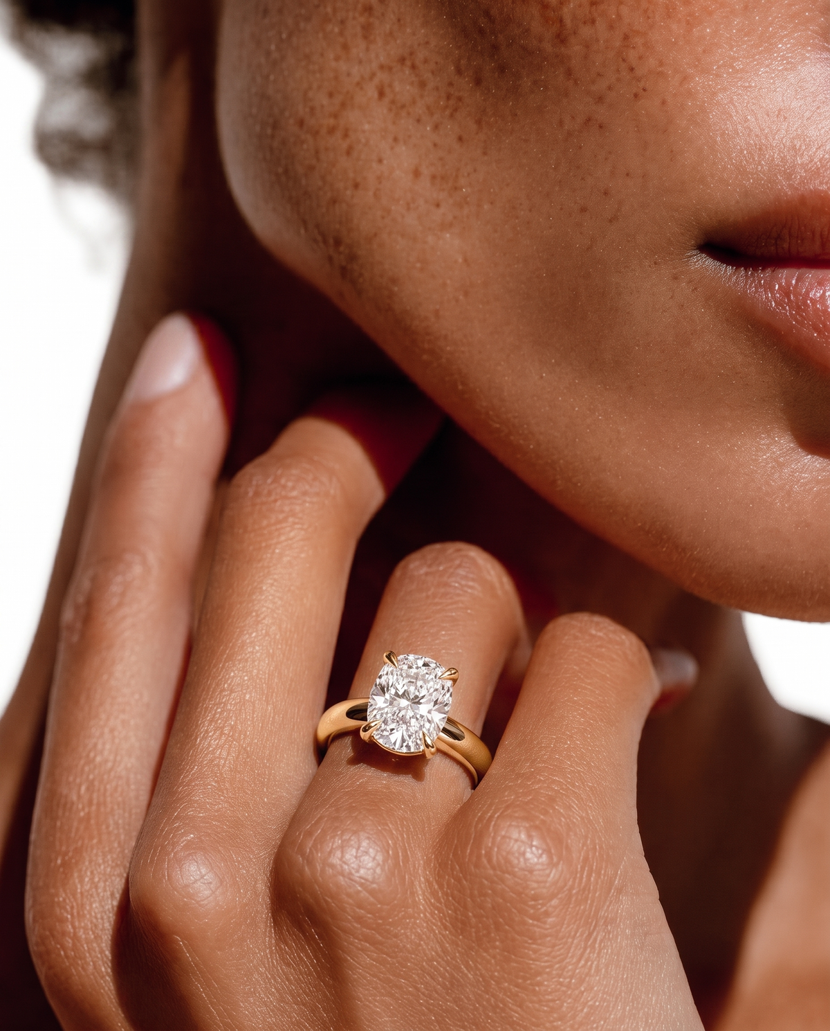 color_10K_YG, color_14K_YG &&A close-up lifestyle shot of a model wearing a yellow gold ring with a round brilliant-cut diamond. The ring is shown on the model's ring finger, with her hand resting near her chin against a bright white background.