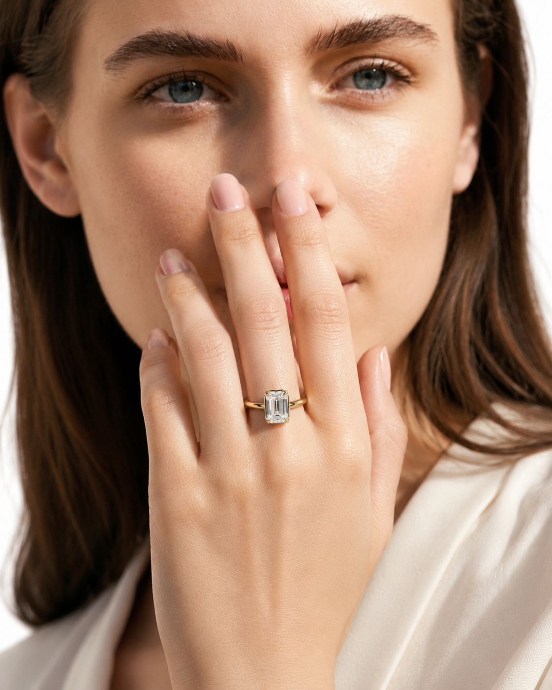 color_10K_YG, color_14K_YG &&A close-up lifestyle shot of a woman wearing a gold ring with a rectangular clear gemstone on her finger, with her hand covering part of her face.