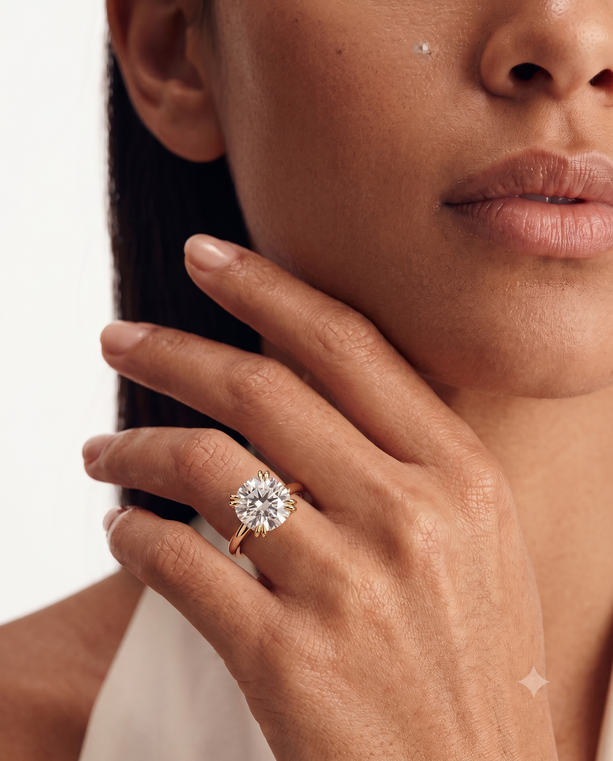 color_10K_YG, color_14K_YG &&A close-up lifestyle shot of a model wearing a rose gold engagement ring with a round brilliant-cut diamond. The ring is shown on her finger, with her hand resting near her face against a clean white background.