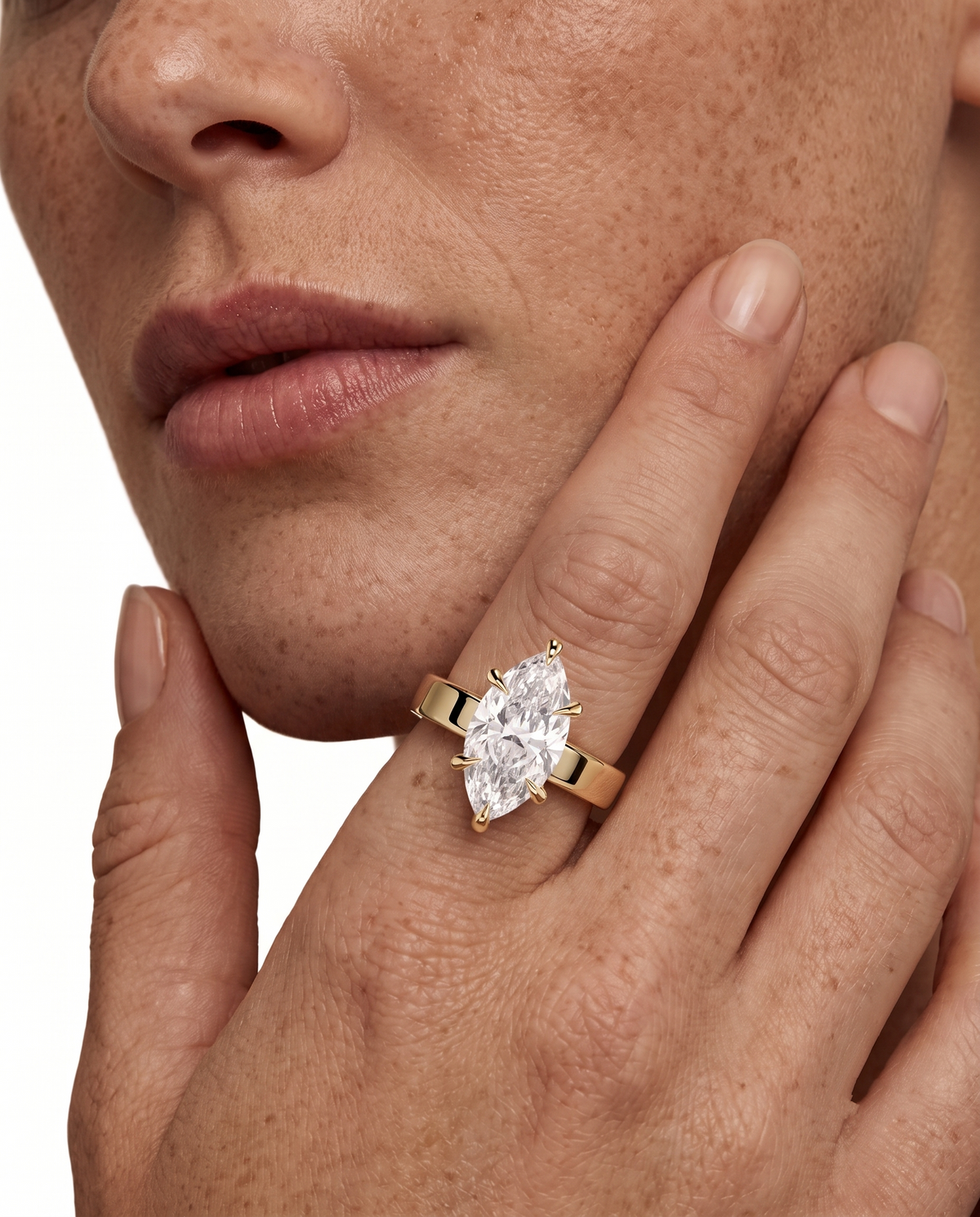 color_10K_YG, color_14K_YG &&A close-up lifestyle shot of a model wearing a gold ring with a marquise-cut clear gemstone on her finger, with her hand resting against her cheek.