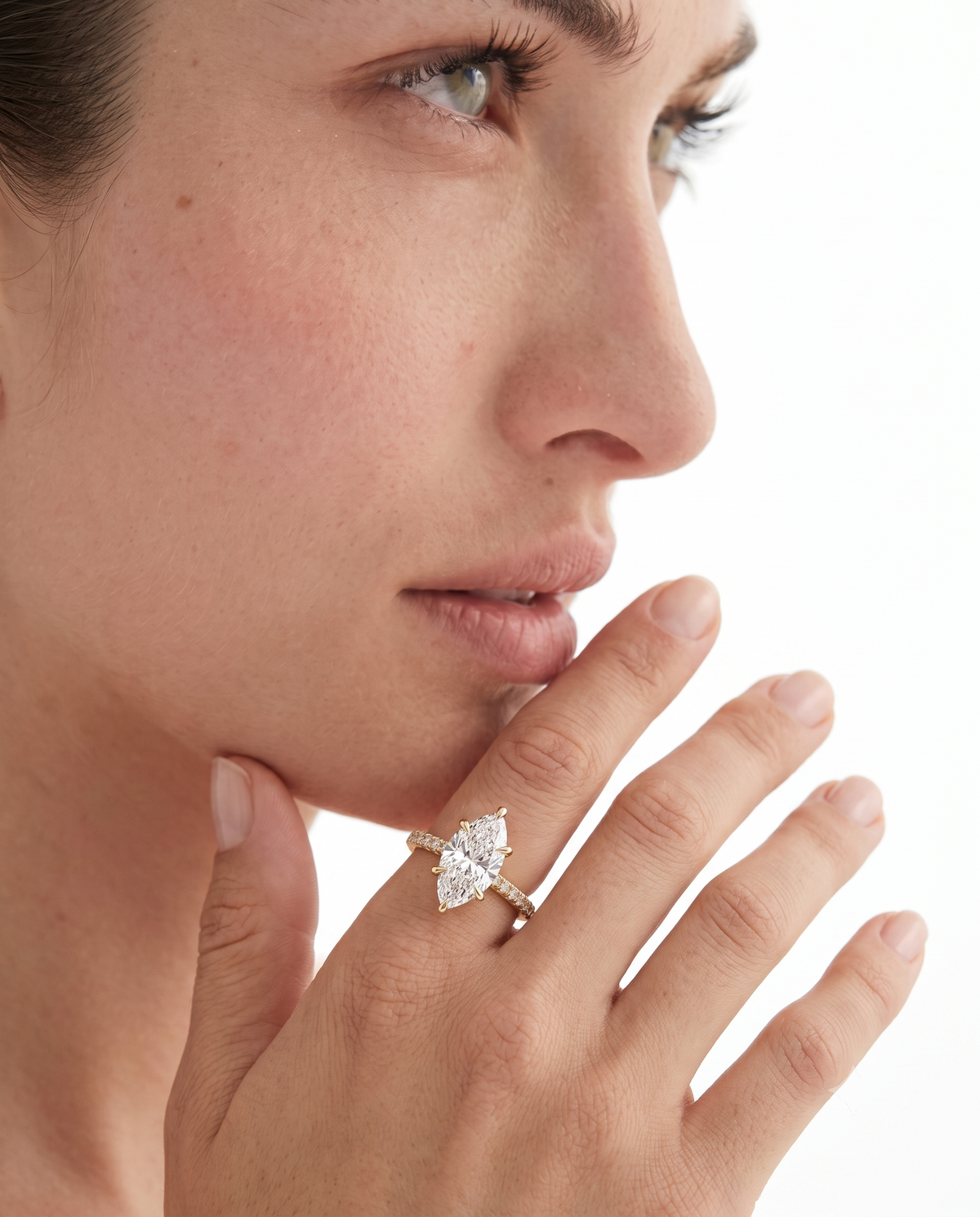color_10K_YG, color_14K_YG &&A close-up of a woman's face and hand wearing a diamond ring with a gold band on her ring finger, set against a clean white background.