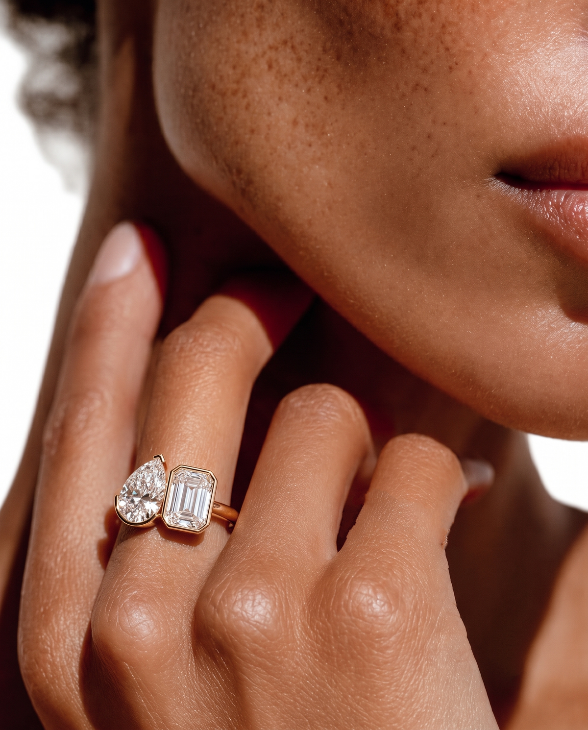 color_10K_YG, color_14K_YG &&A close-up lifestyle shot of a model's hand wearing a rose gold ring with a pear-cut diamond and an emerald-cut diamond.