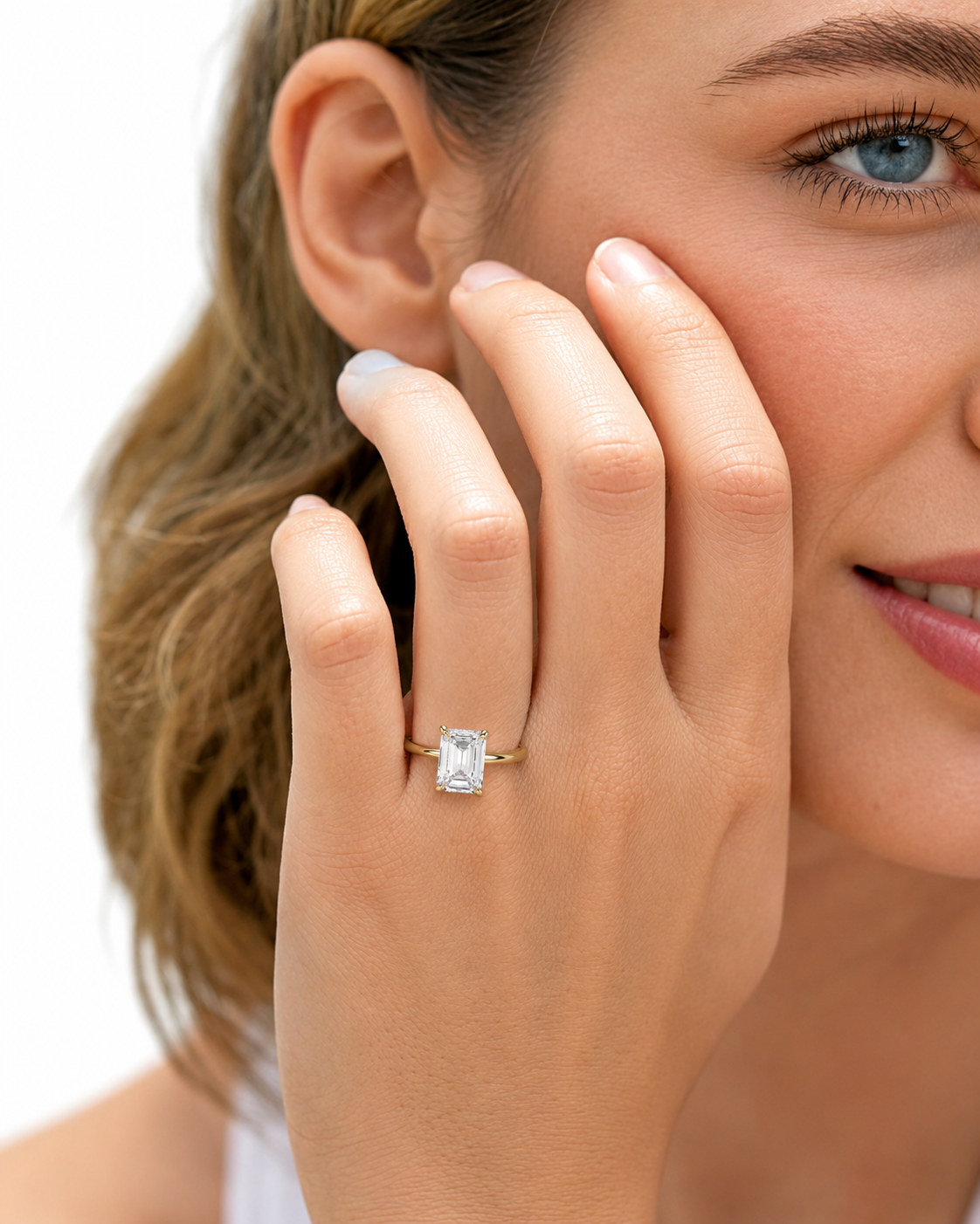 color_10K_YG, color_14K_YG &&
A close-up lifestyle shot of a woman wearing a yellow gold ring with a rectangular clear gemstone on her finger, with her hand resting against her cheek against a white background.