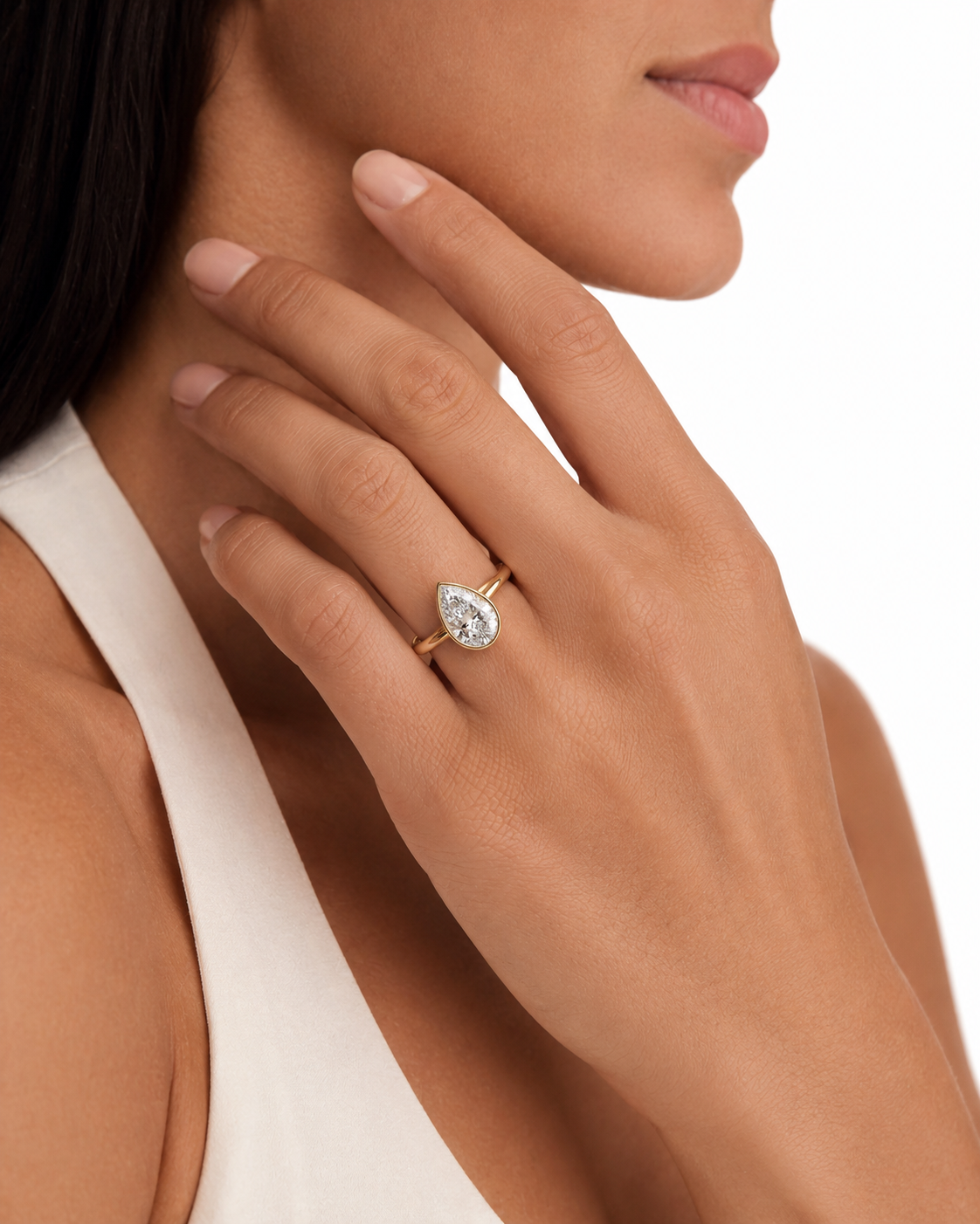 color_10K_YG, color_14K_YG &&A close-up lifestyle shot of a model wearing a gold and diamond pear-cut ring on her finger, with her hand resting near her neck against a clean white background.