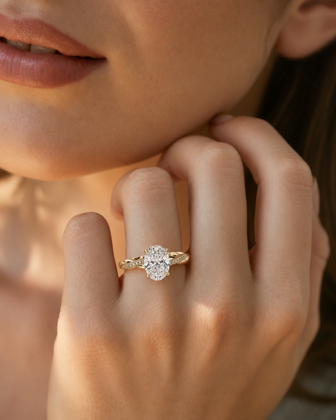 color_10K_YG, color_14K_YG &&A close-up lifestyle shot of a woman's hand wearing a yellow gold ring with a large round-cut diamond center stone and smaller diamonds on the shoulders, set against a warm, softly lit background.